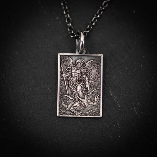 A rectangular pendant featuring an engraved image of a winged figure, possibly a saint or angel, with a battle scene in the background.