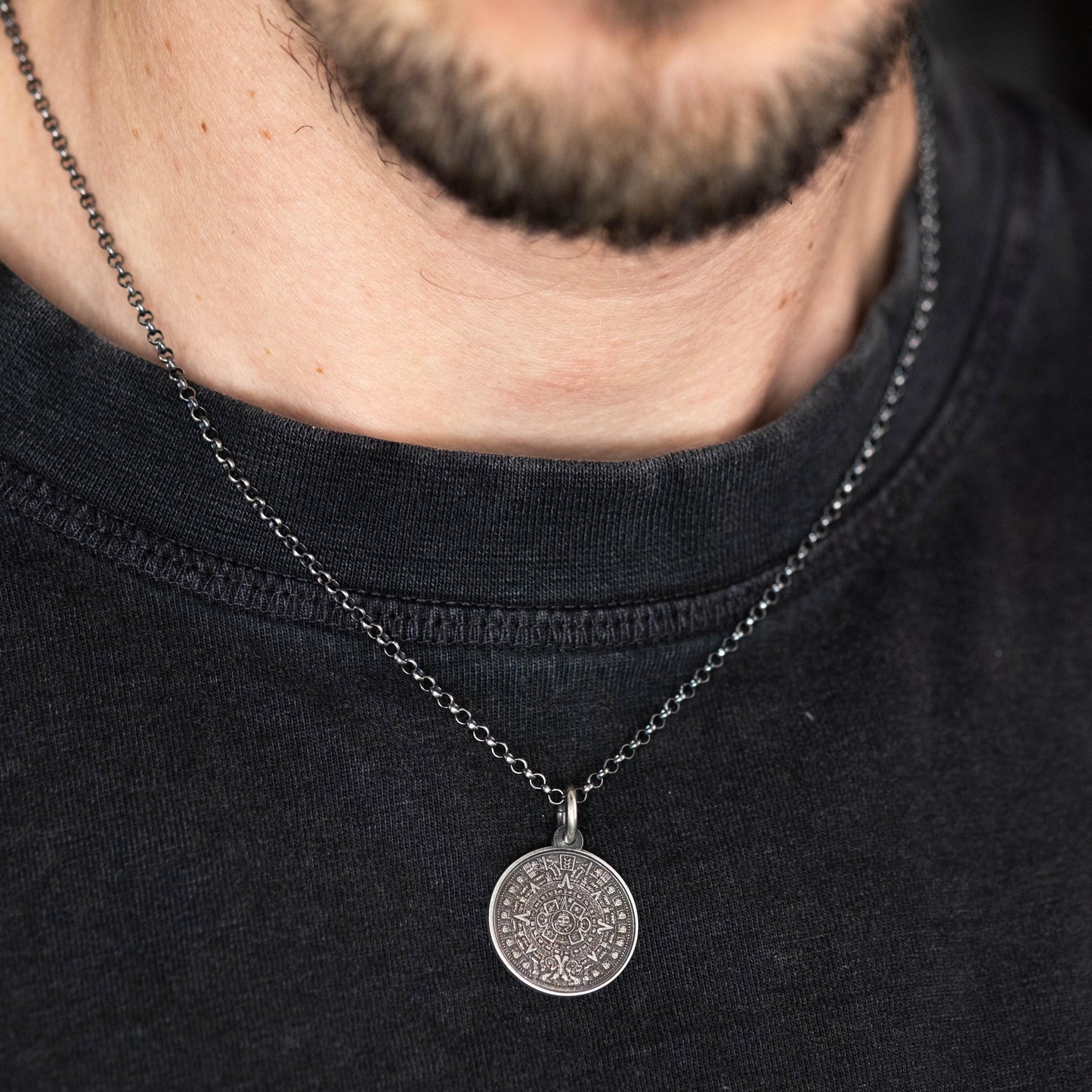 A close-up view of a person wearing a black t-shirt and a silver necklace with a pendant.