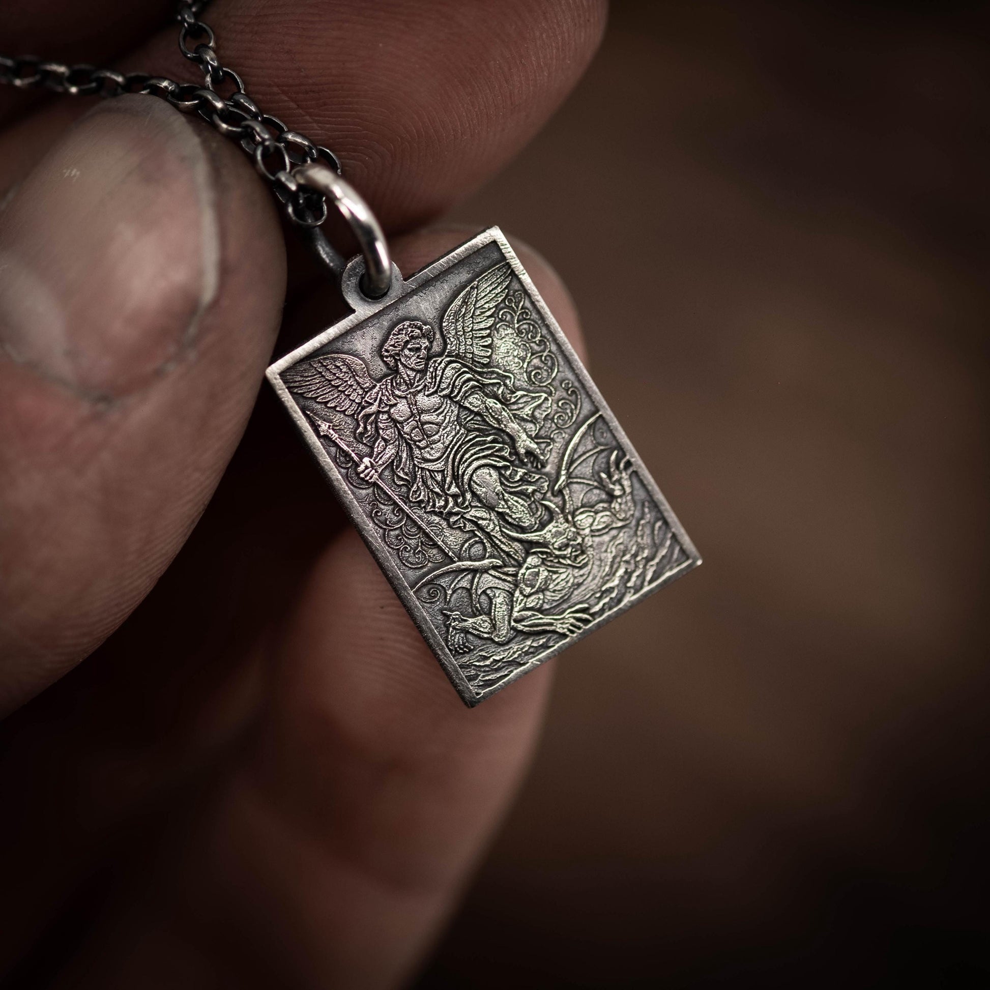 A person's hand holding a silver-colored pendant with an intricate design depicting a winged figure.