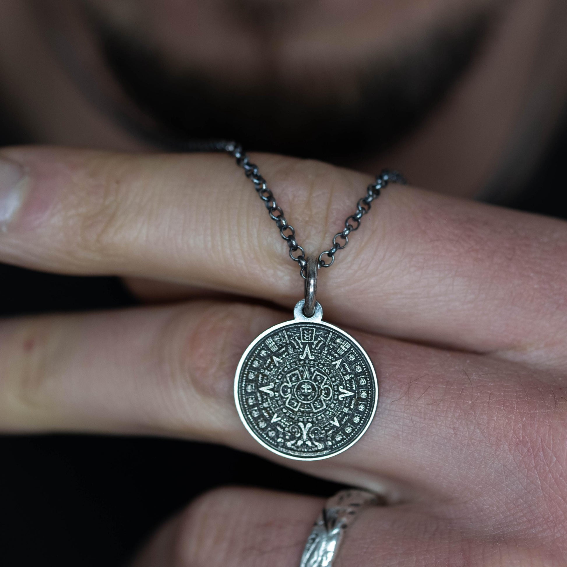 A person is holding a silver pendant with an intricate design on it, which appears to be a piece of jewelry.