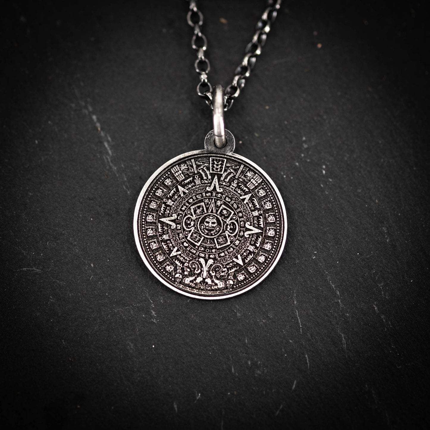 A silver pendant necklace with an intricate circular design featuring a calendar-like pattern.