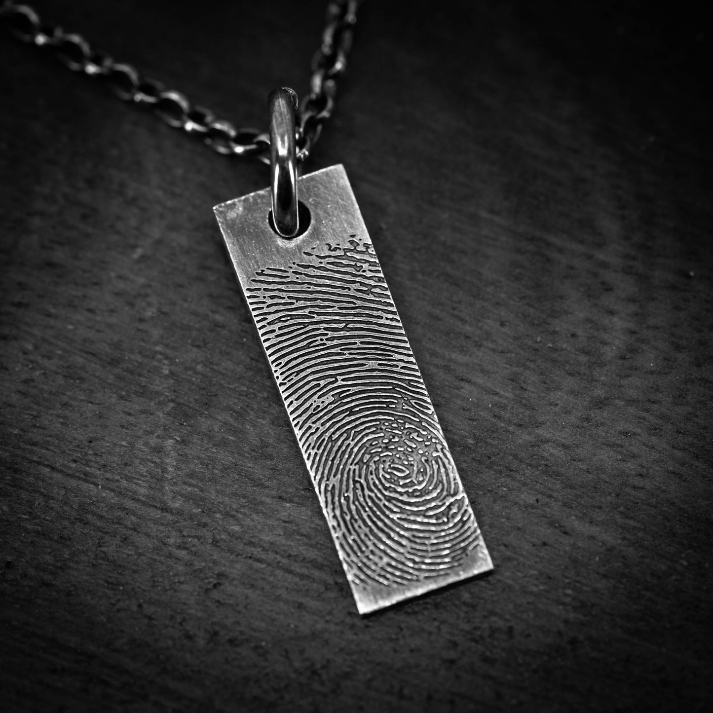 A silver pendant with a fingerprint design on it, hanging from a chain.