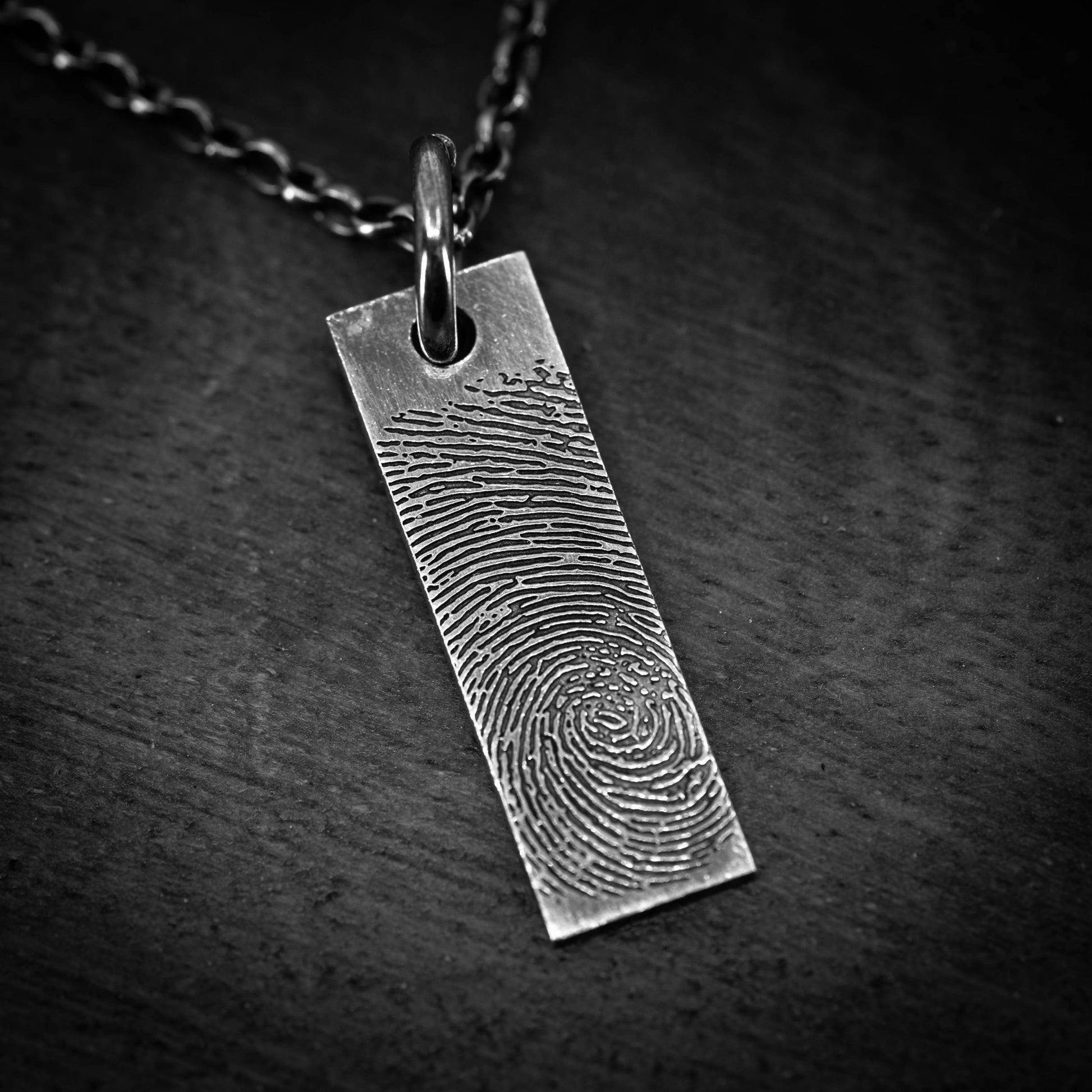 A silver pendant with a fingerprint design on it, hanging from a chain.