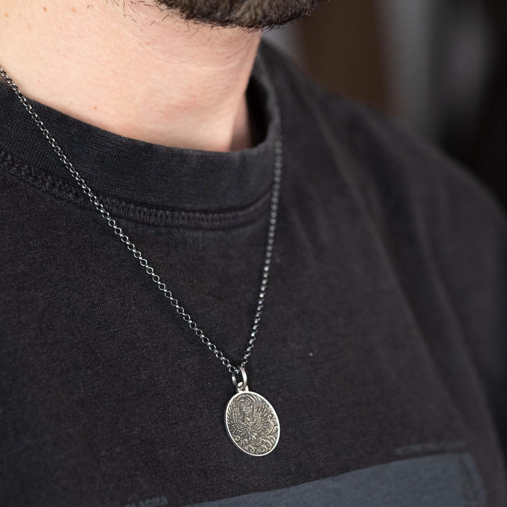 A close-up of a person wearing a black t-shirt with a silver necklace featuring a pendant.