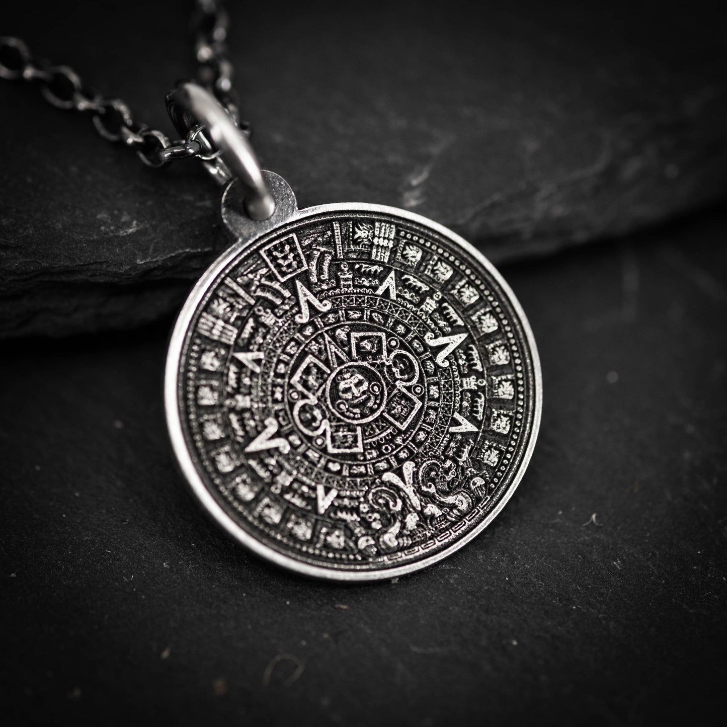 A pendant in the shape of a calendar, featuring intricate designs and symbols, is displayed against a dark background.