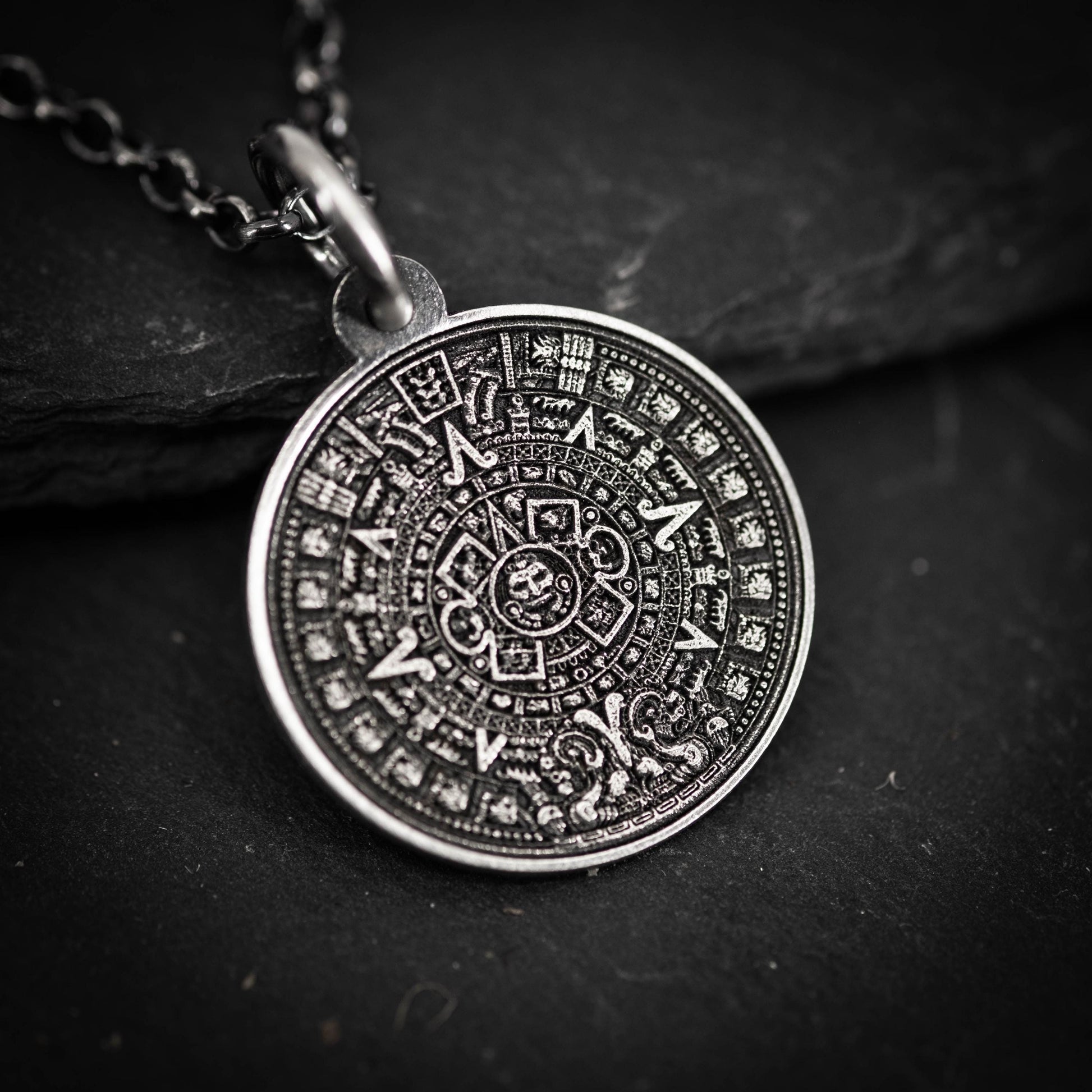 A pendant in the shape of a calendar, featuring intricate designs and symbols, is displayed against a dark background.