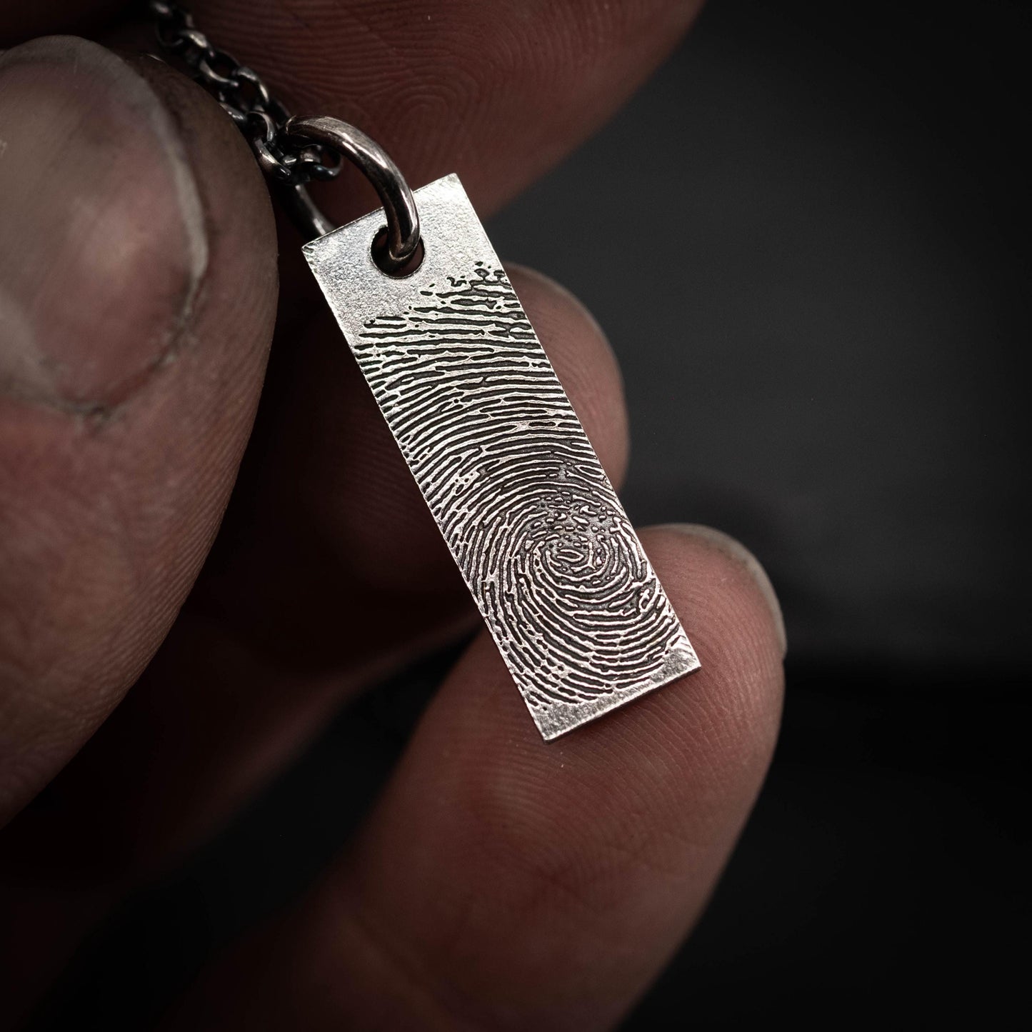 A person's hand holding a silver pendant with a fingerprint design on it.