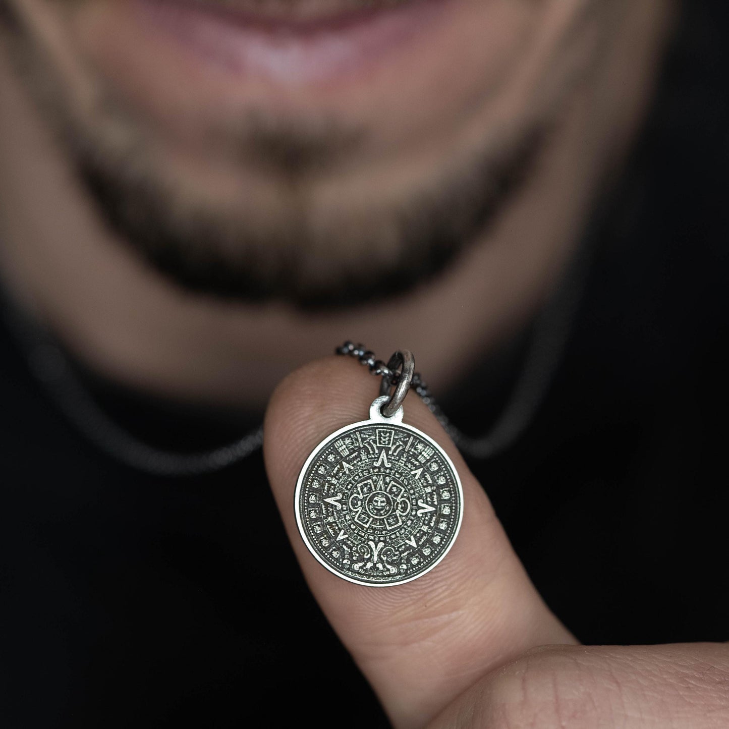 A person is holding a silver pendant with an intricate design on it, which is attached to a chain around their finger.