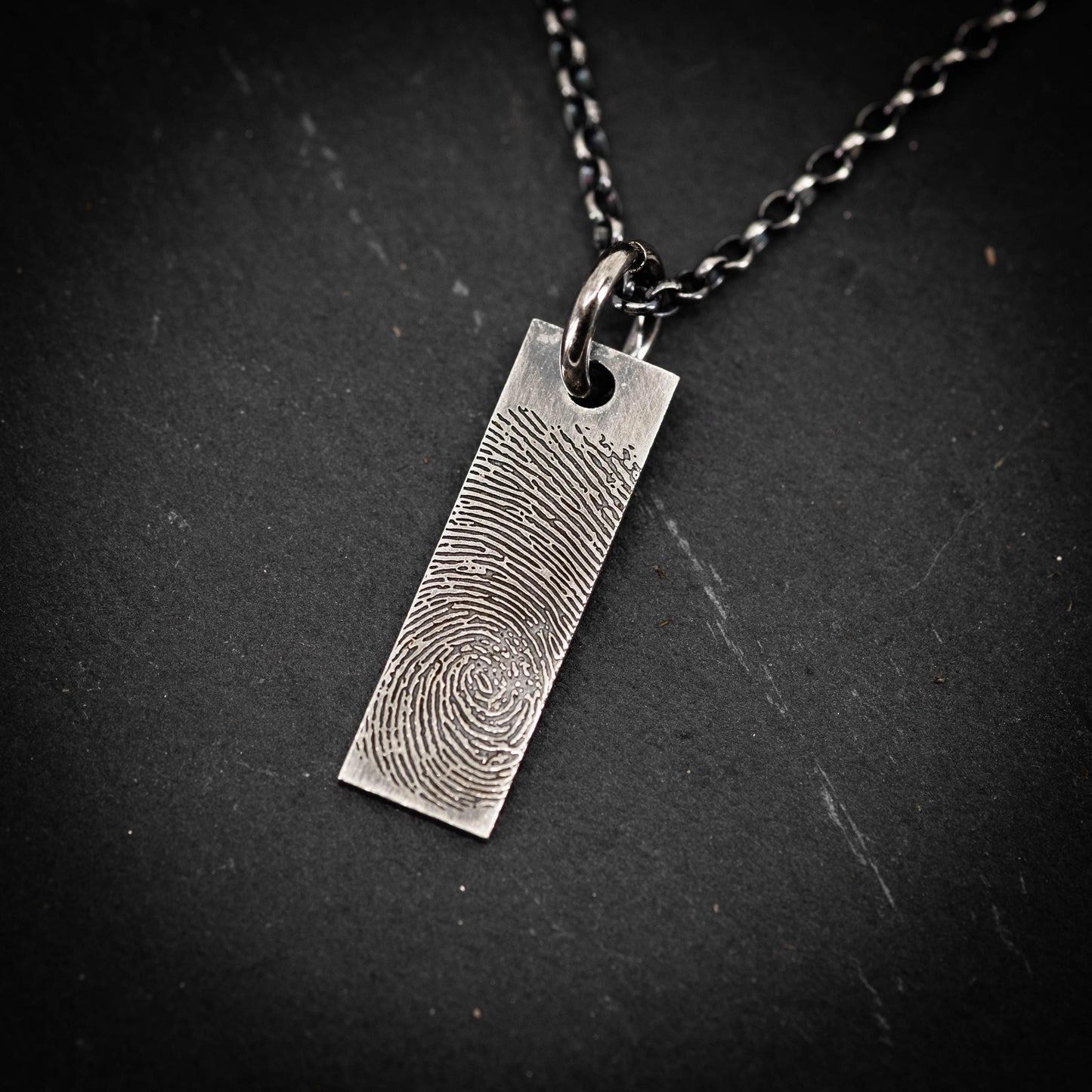 A silver necklace pendant with a fingerprint design on it.