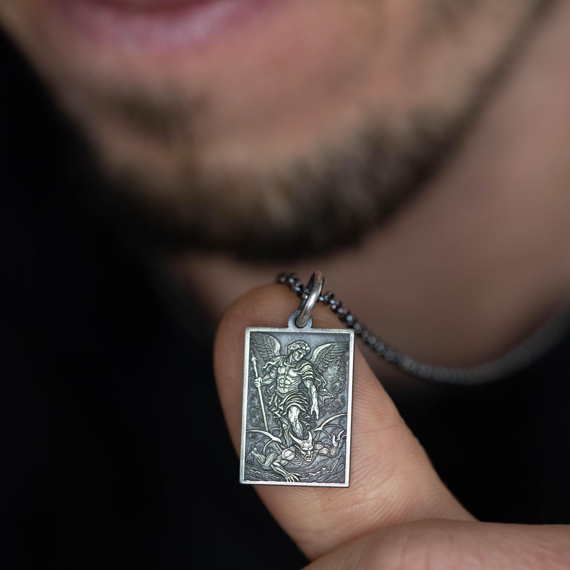 A person is holding a small rectangular pendant with an image of a winged figure, possibly a saint or angel, on it.