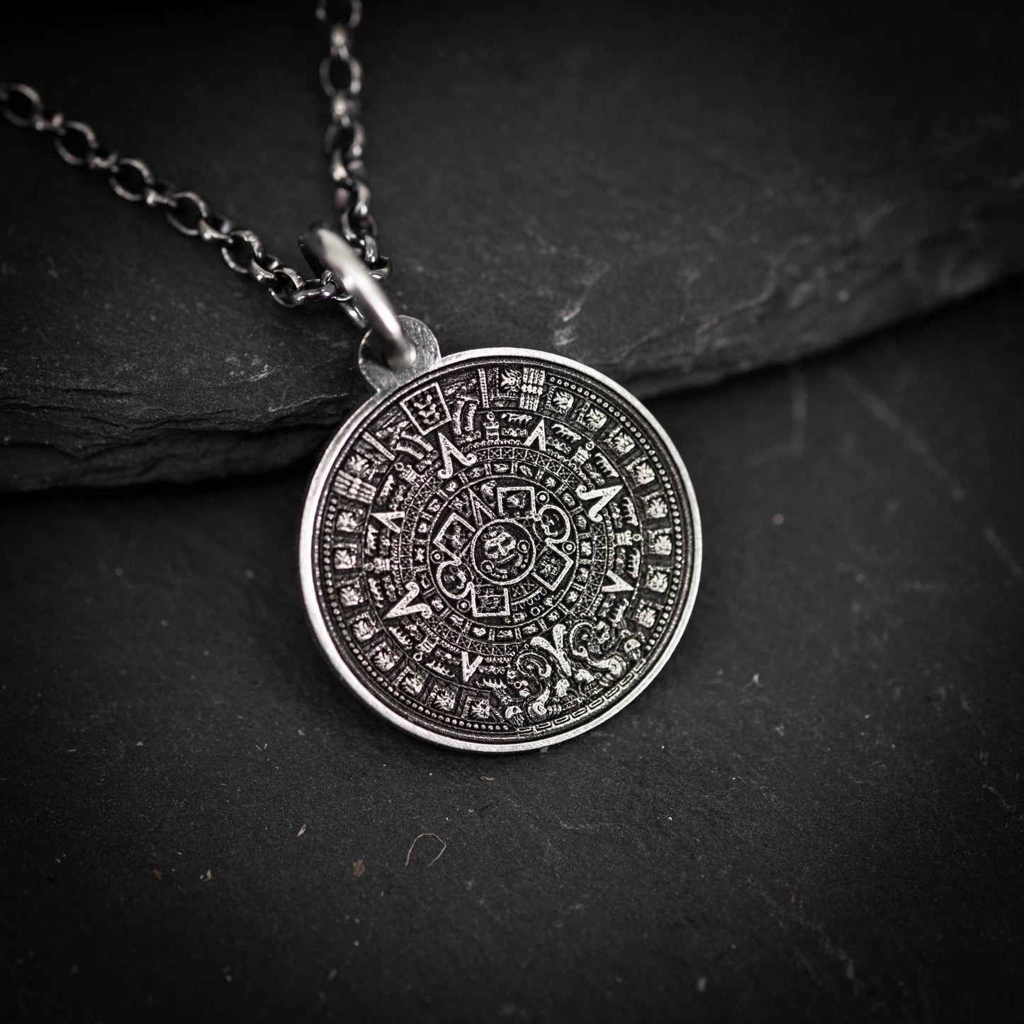 A silver pendant necklace with an intricate circular design on a dark surface.