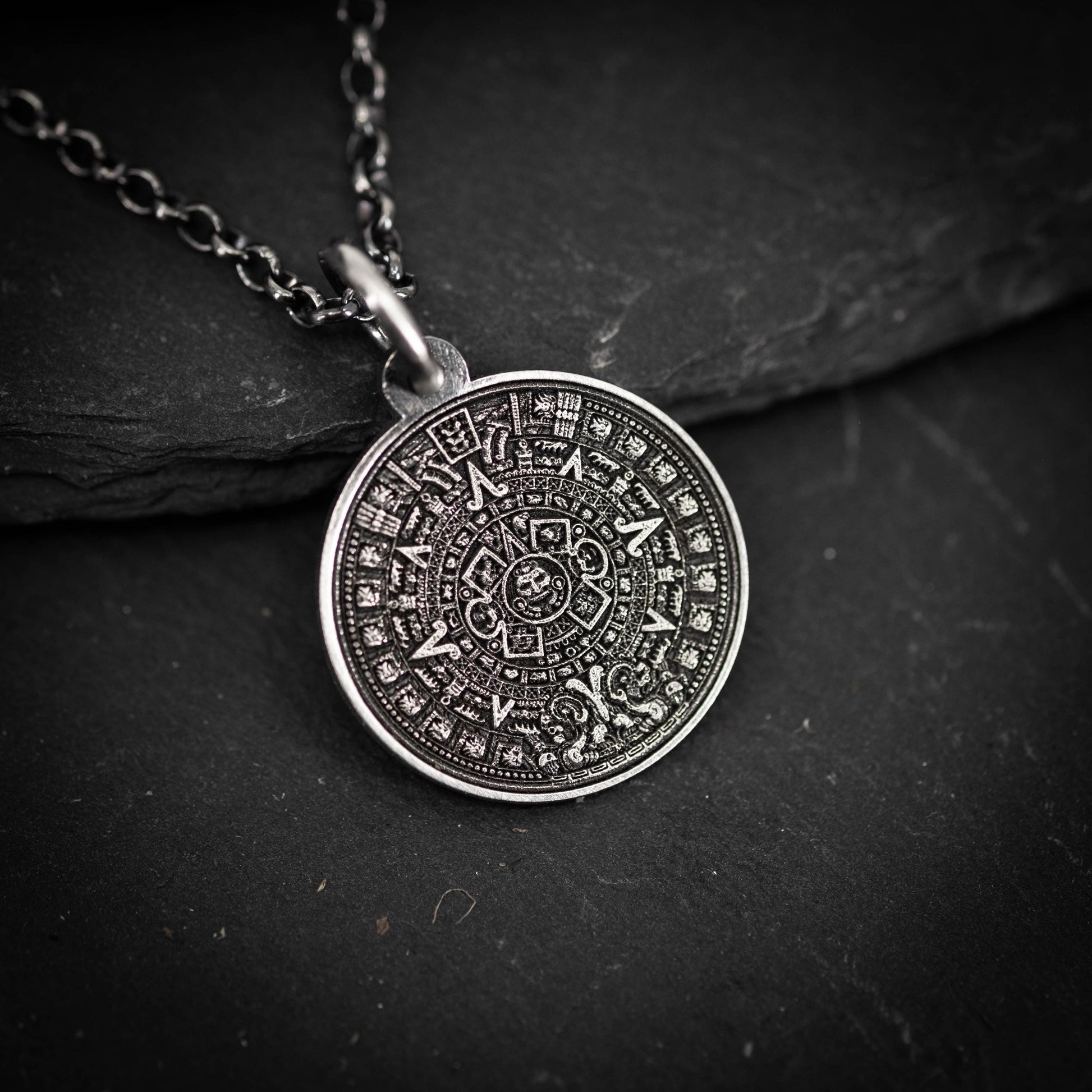 A silver pendant necklace with an intricate circular design on a dark surface.