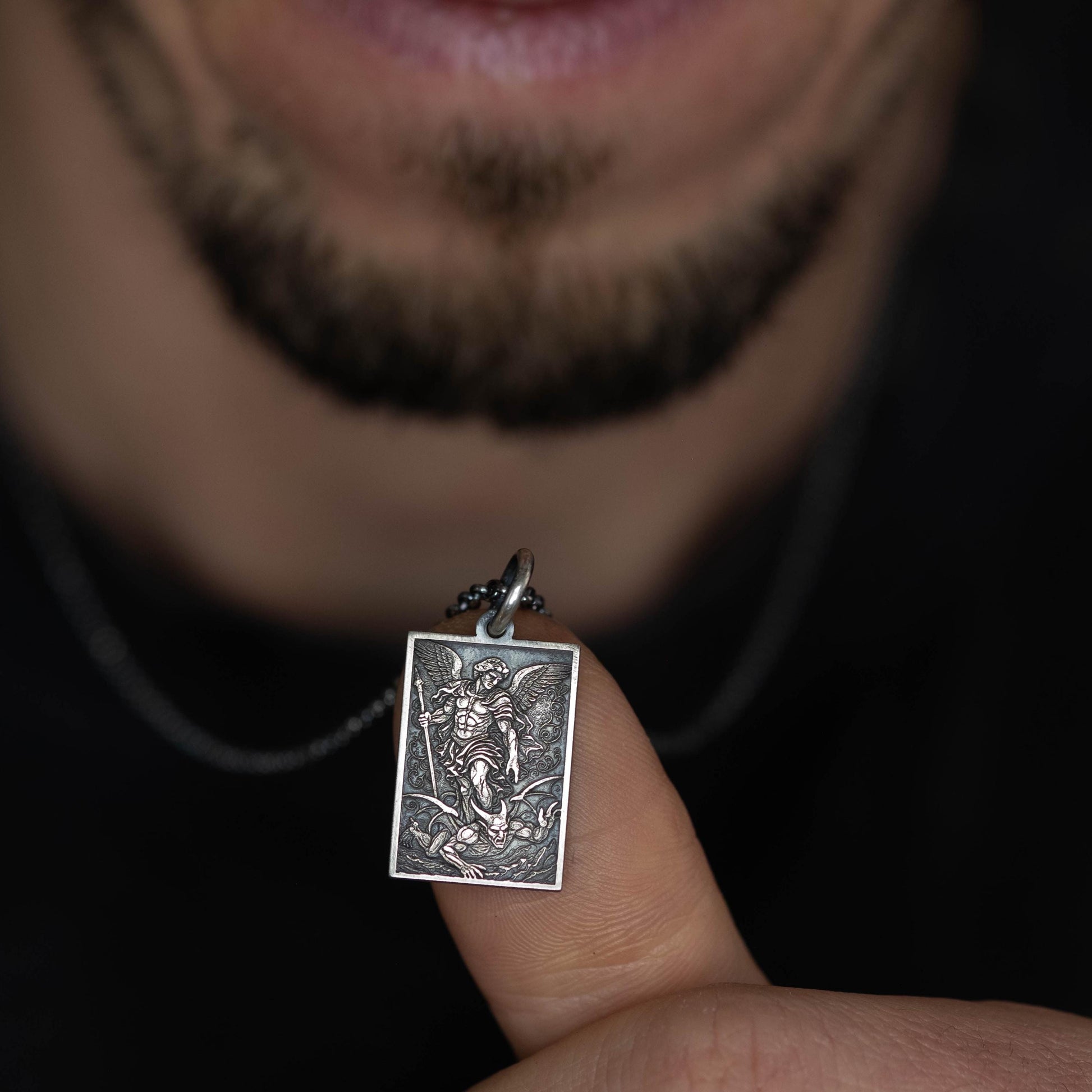 A person is holding a small pendant with an image of a saint or religious figure on it.