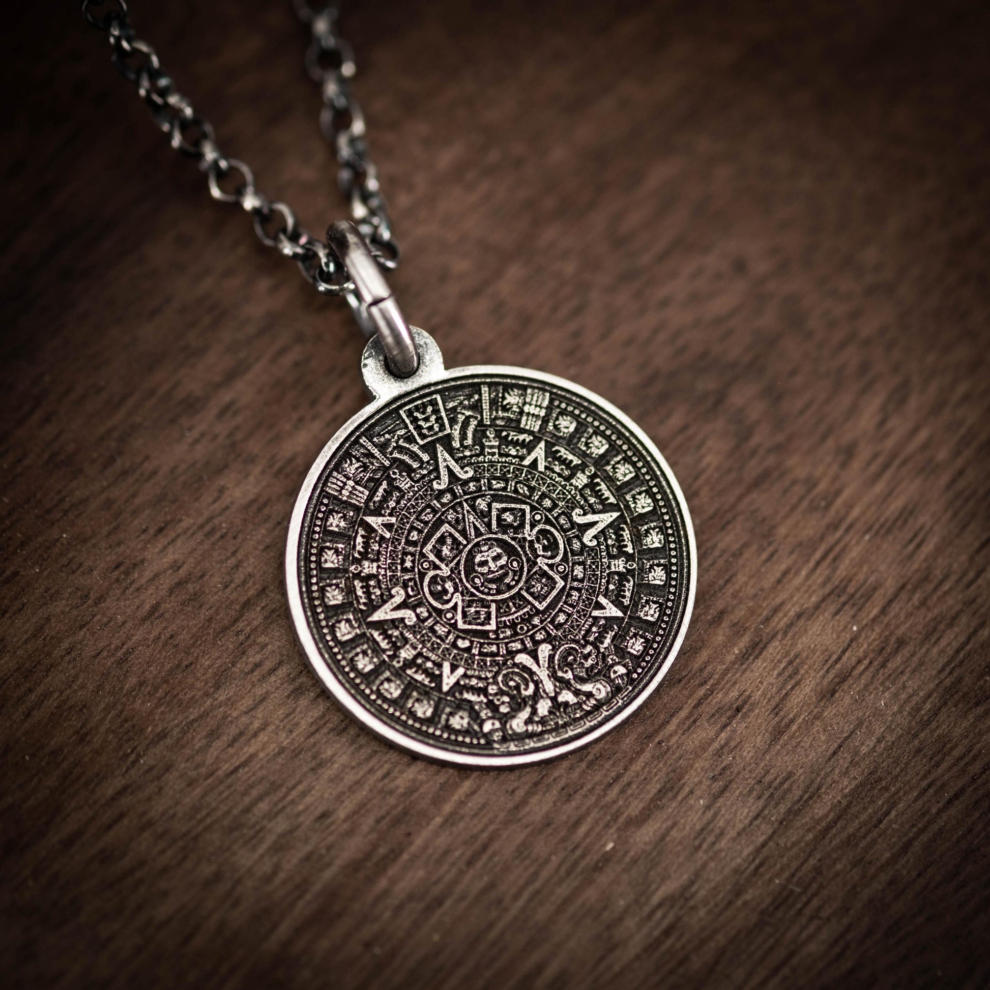 A silver pendant necklace with an intricate circular design featuring a calendar or calendar-like pattern.