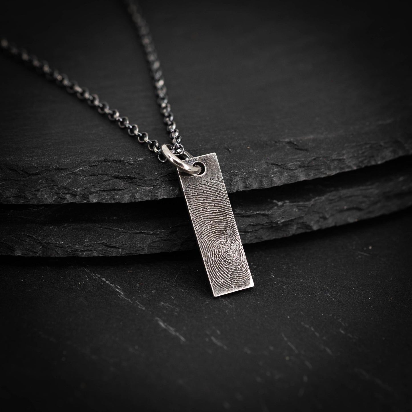 A silver necklace with a rectangular pendant featuring a fingerprint design.