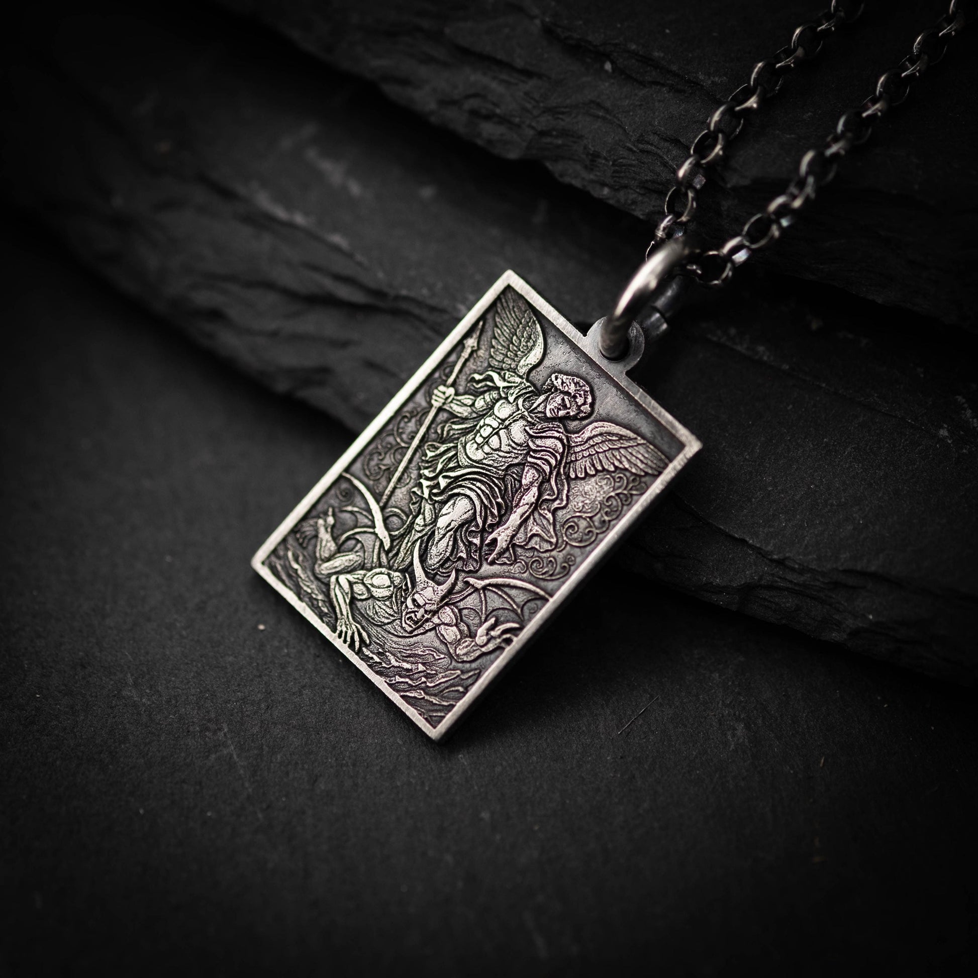 A silver pendant with an intricate design, featuring a winged figure and a detailed background.