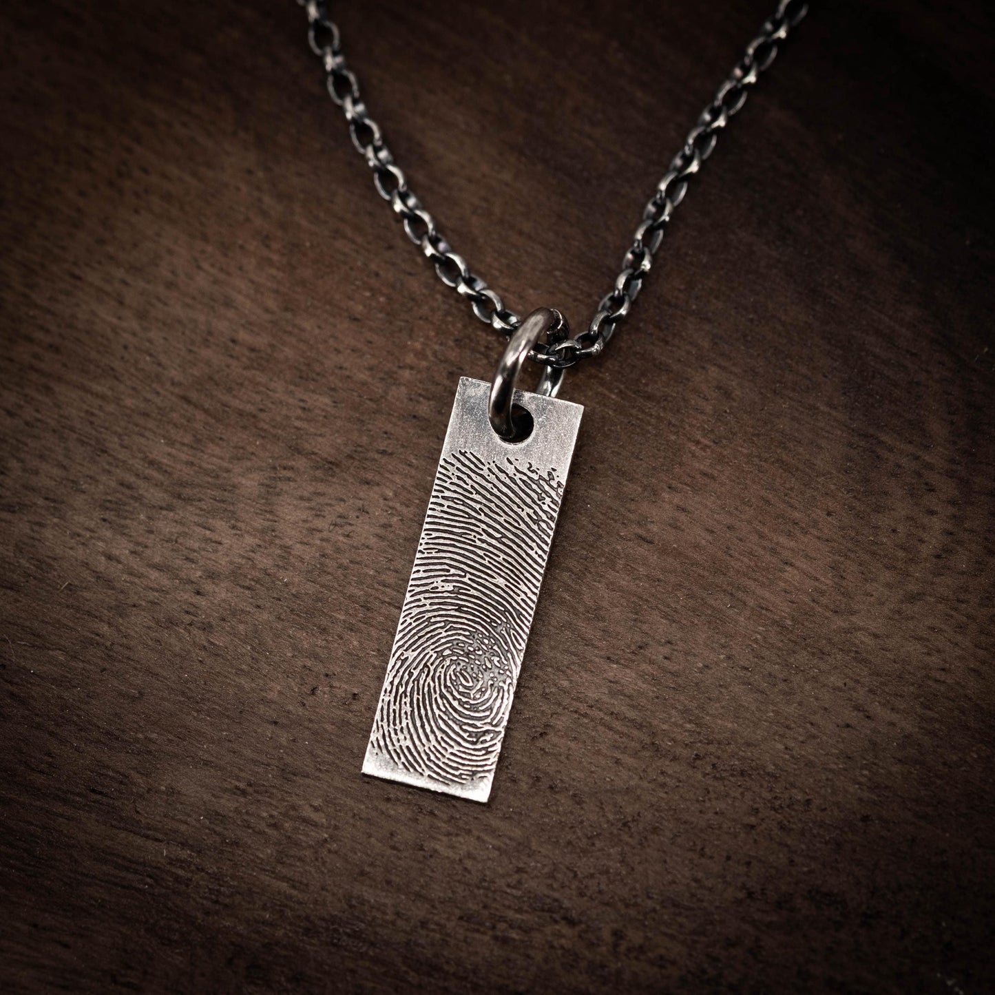 A silver necklace pendant with a fingerprint design.