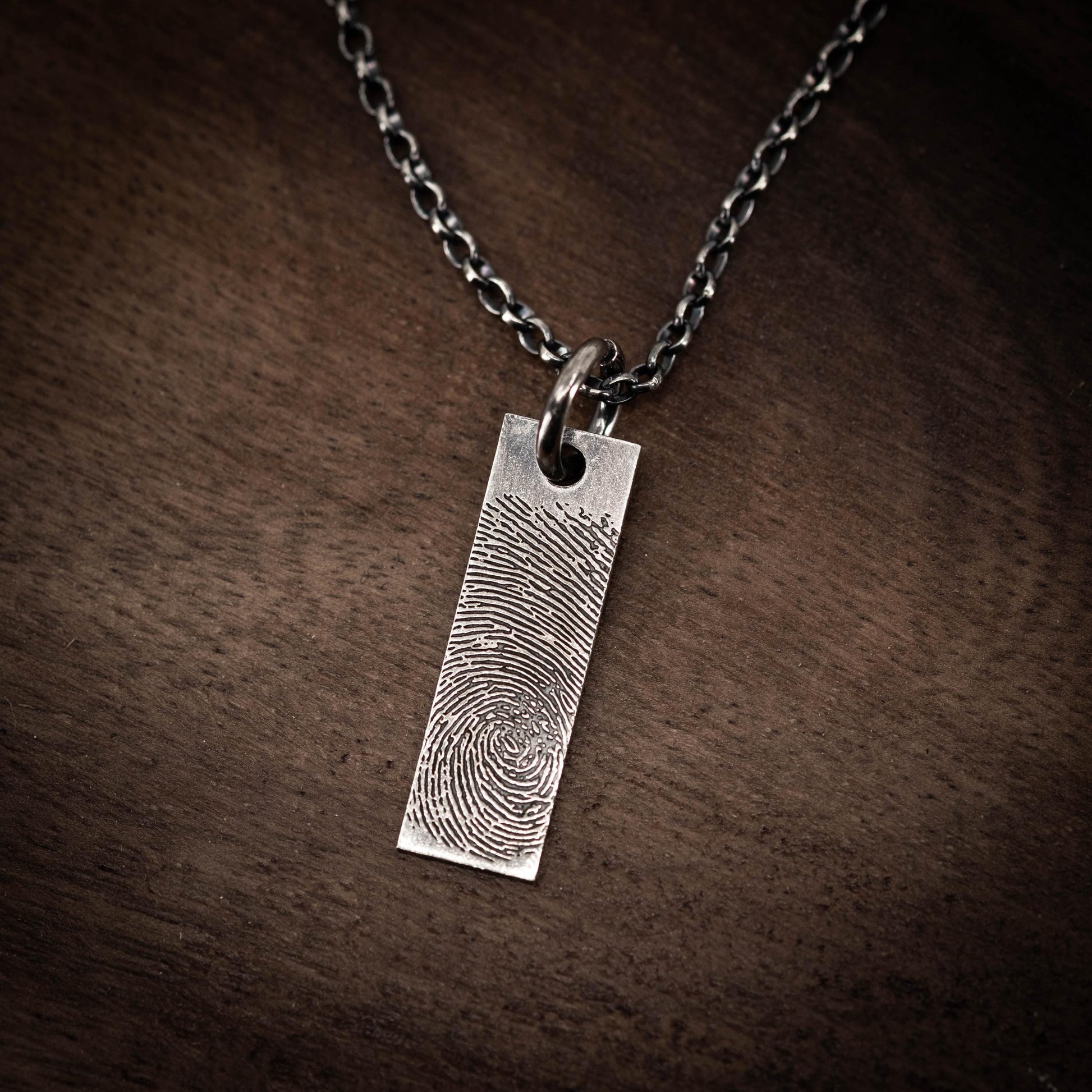 A silver necklace pendant with a fingerprint design.