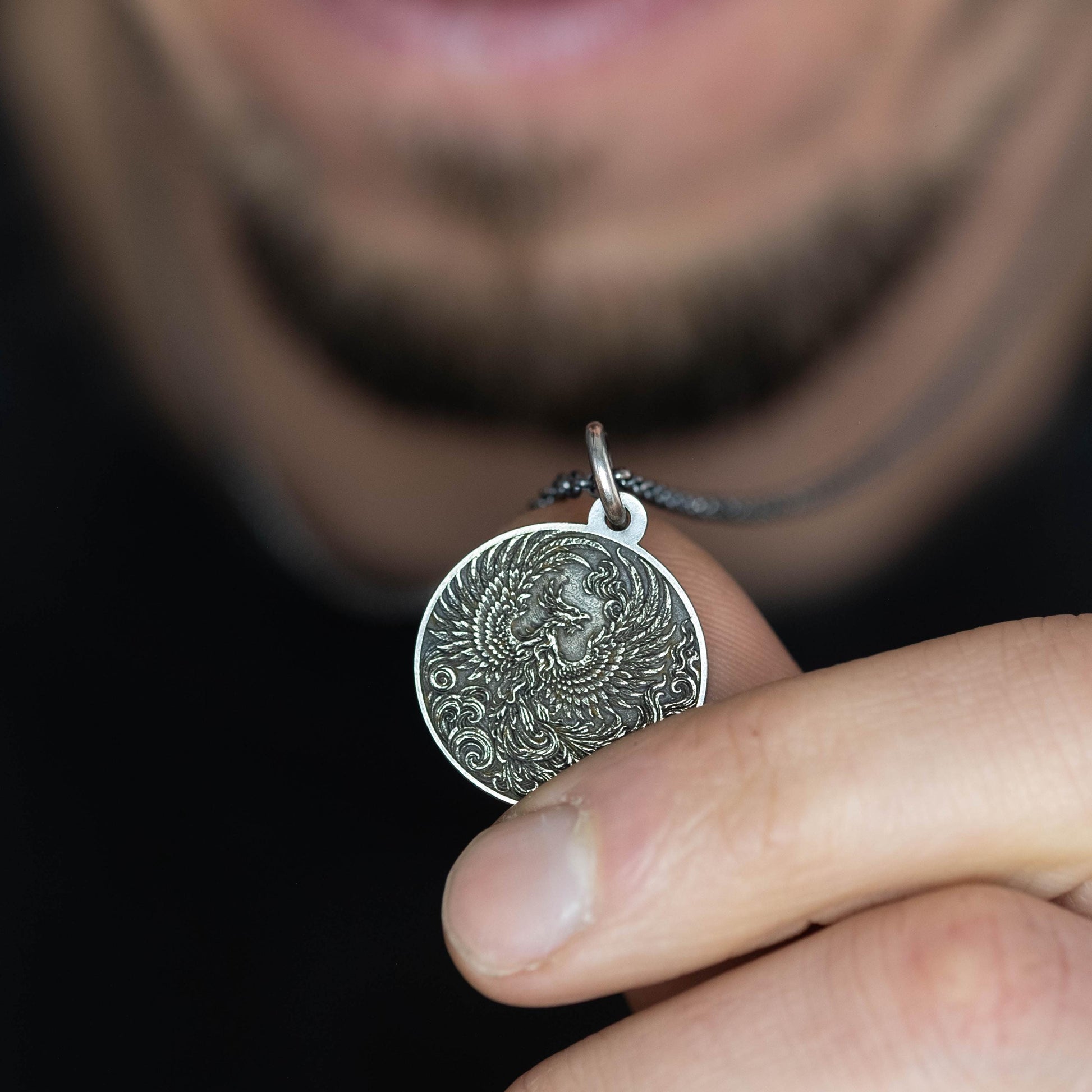 A person is holding a silver pendant with an intricate design on it.