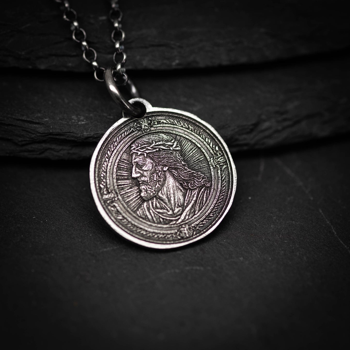 A silver-colored pendant featuring a detailed engraved image of a man's face, possibly depicting Jesus Christ.