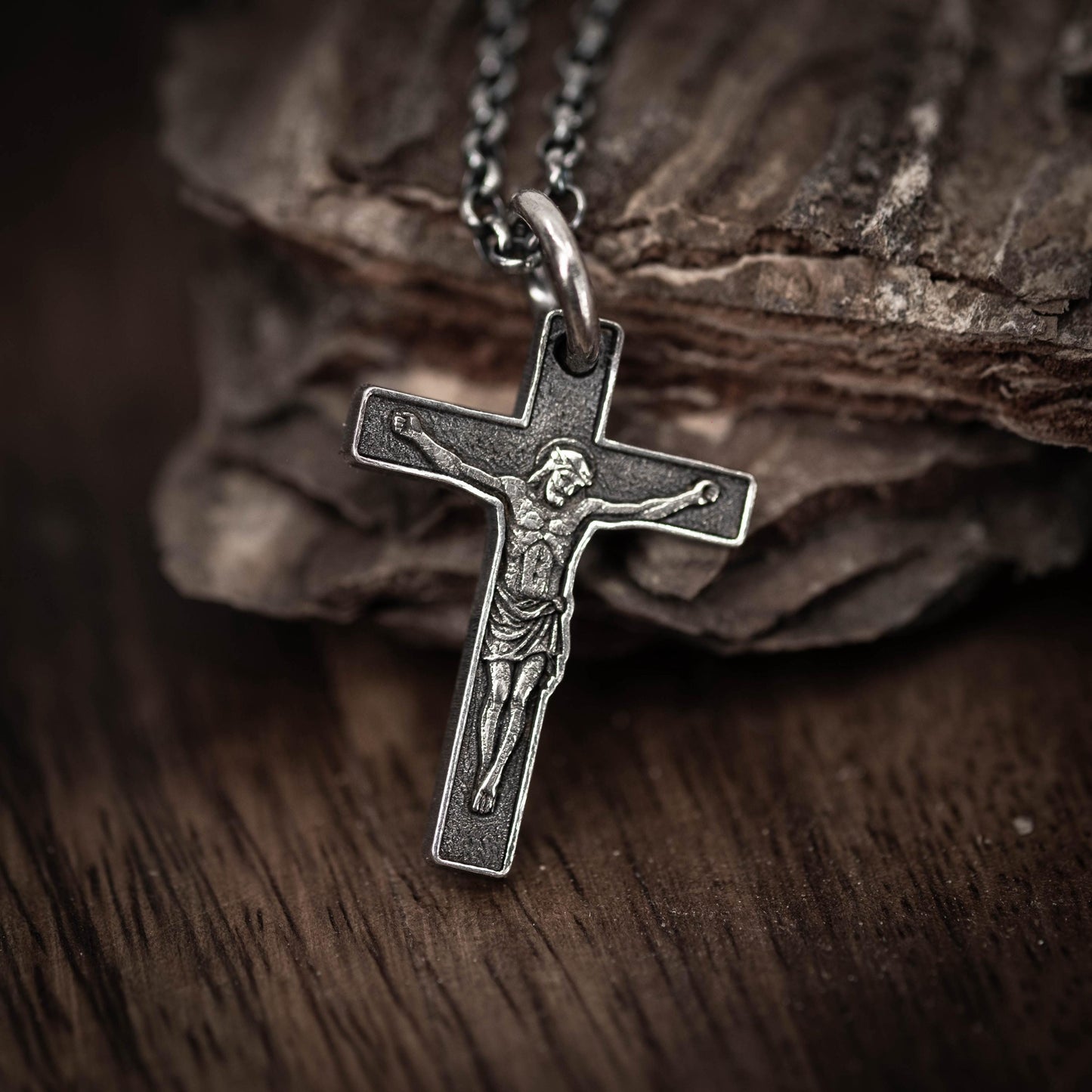 A silver cross pendant with a depiction of Jesus Christ on it, resting on a wooden surface.