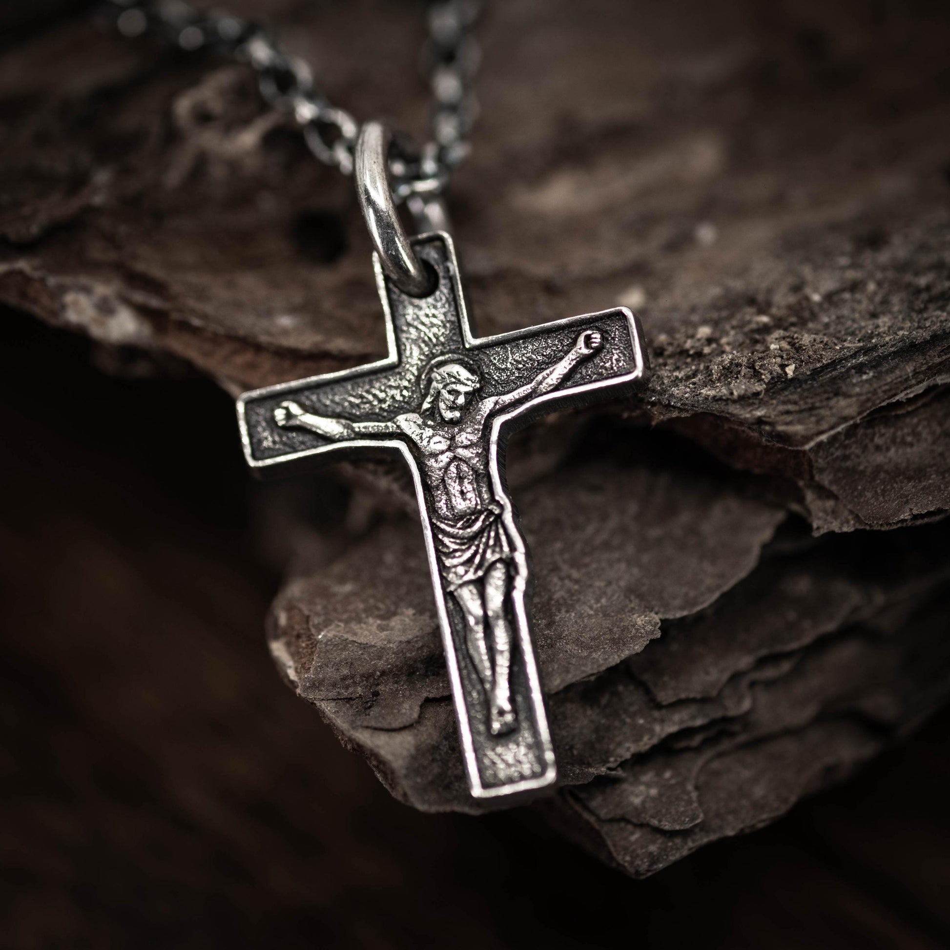 A silver cross pendant with a figure of Jesus Christ on it, hanging on a chain.