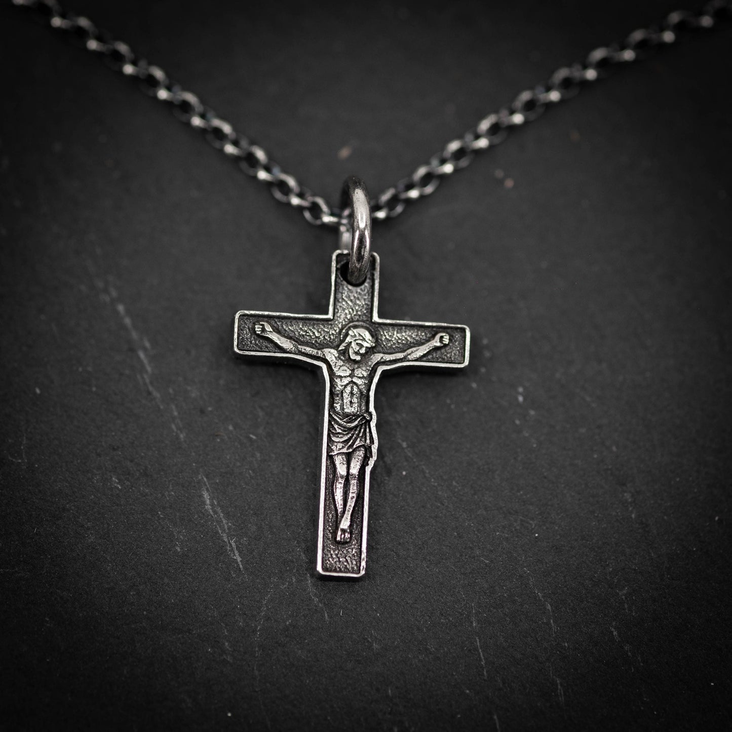 A silver cross pendant with a detailed engraved image of Jesus Christ on the cross.