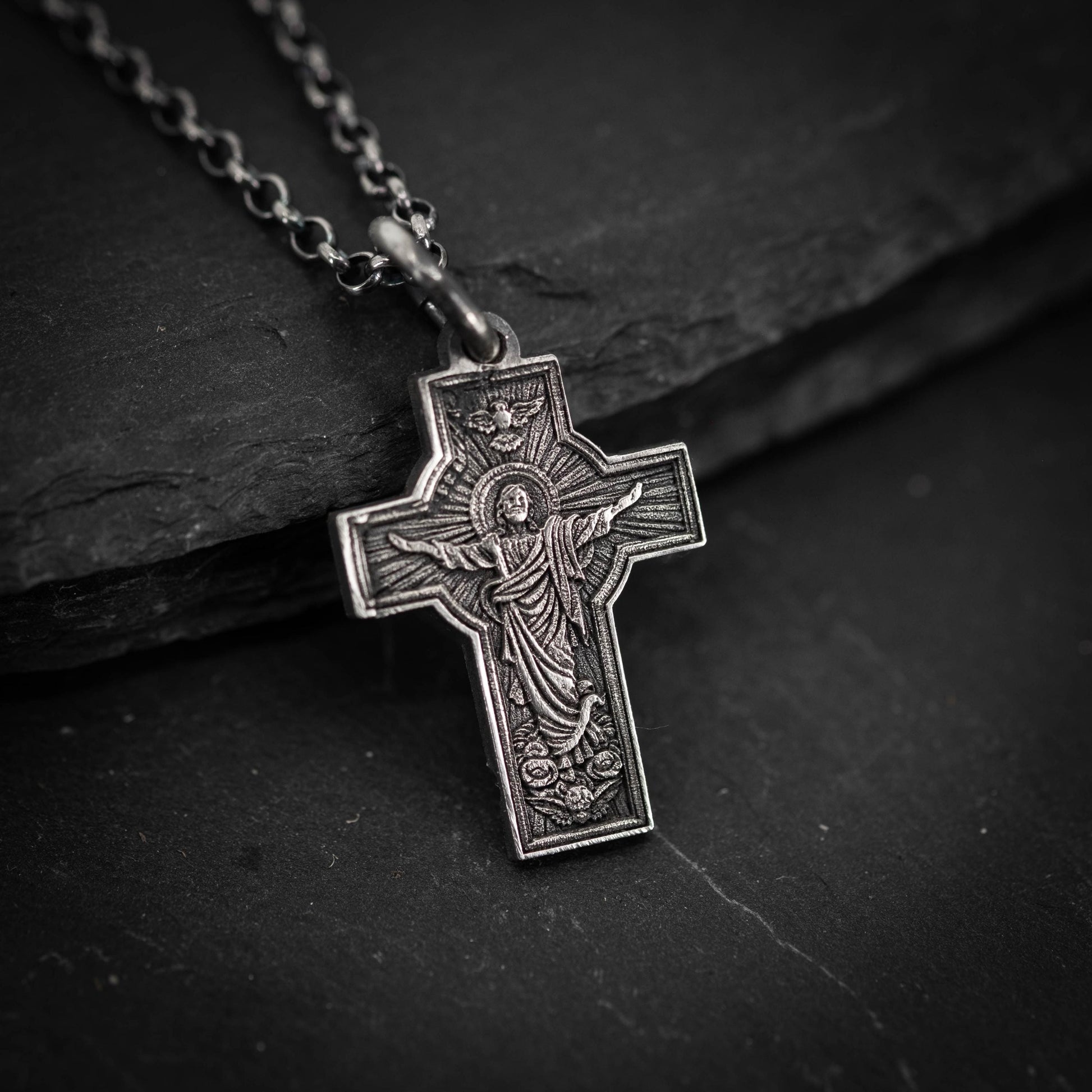 A silver cross pendant with an intricate design, resting on a dark surface.