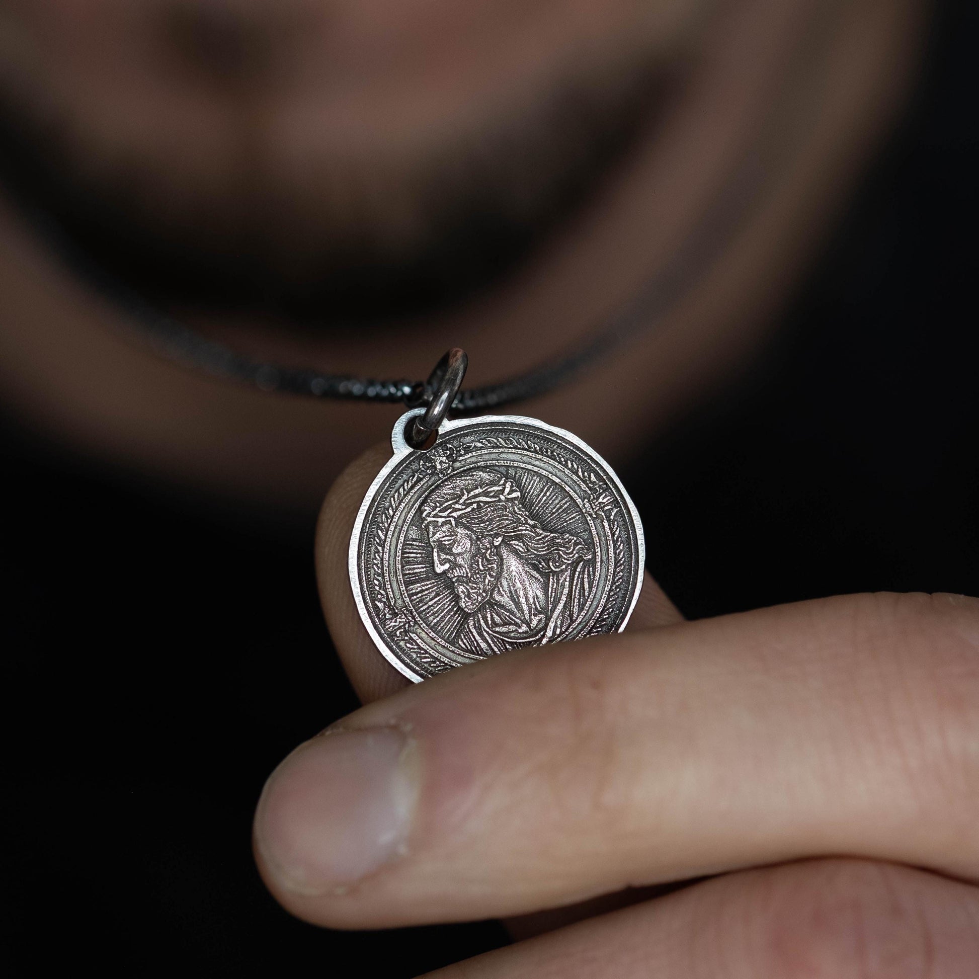 A person is holding a silver-colored pendant with an intricate design on it.