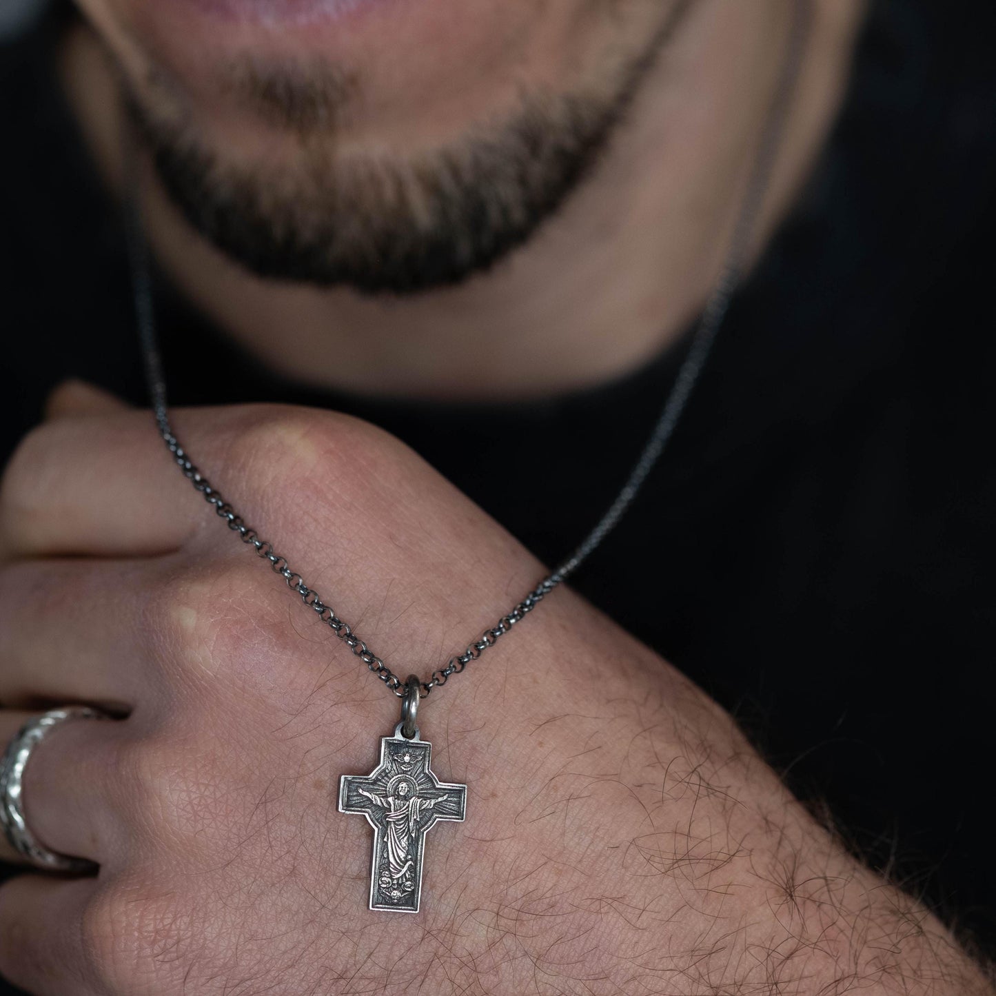 A close-up of a person's hand wearing a silver cross pendant necklace.