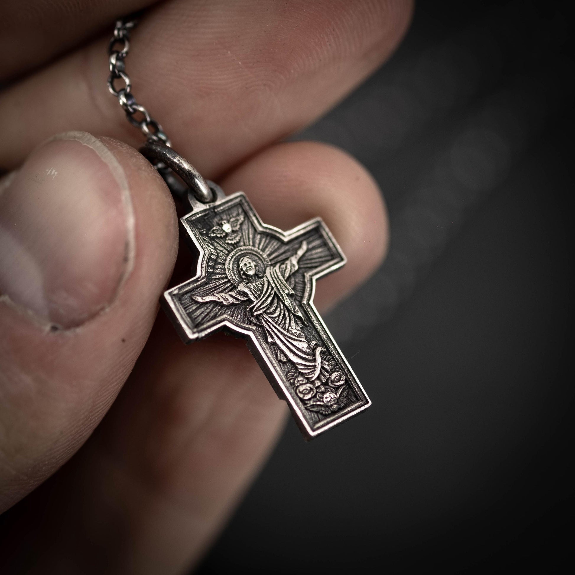 A hand holding a silver cross pendant with an intricate design.