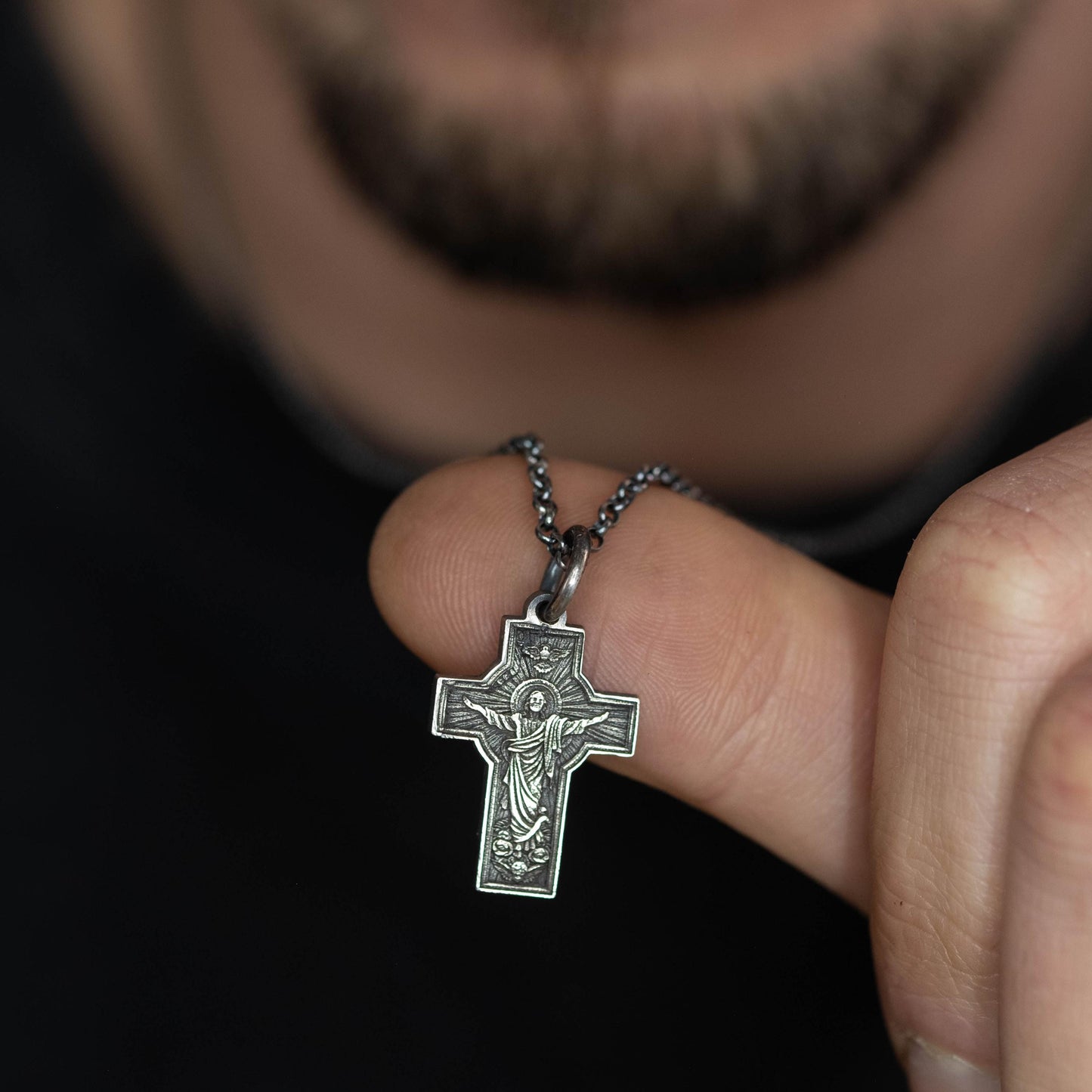 A person is holding a silver cross pendant on their finger.