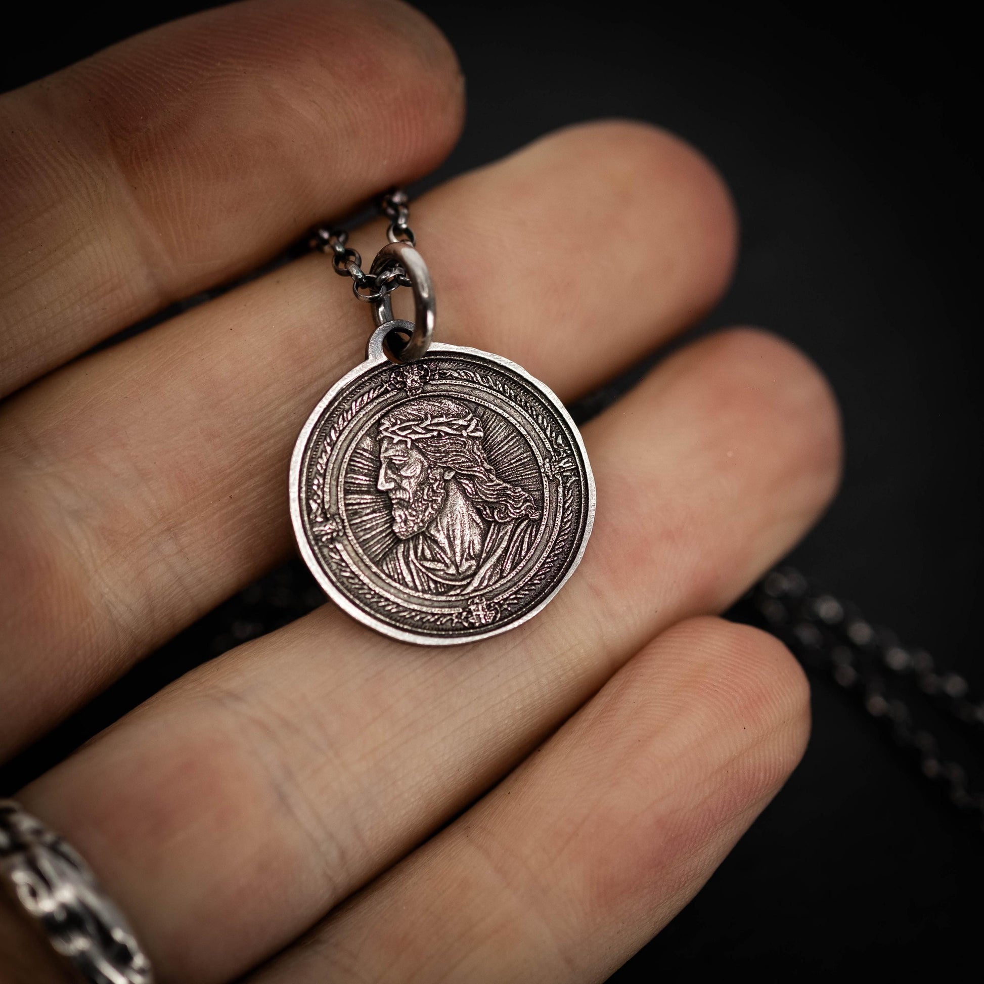 A hand holding a silver pendant with an engraved image of a person, likely a religious figure.