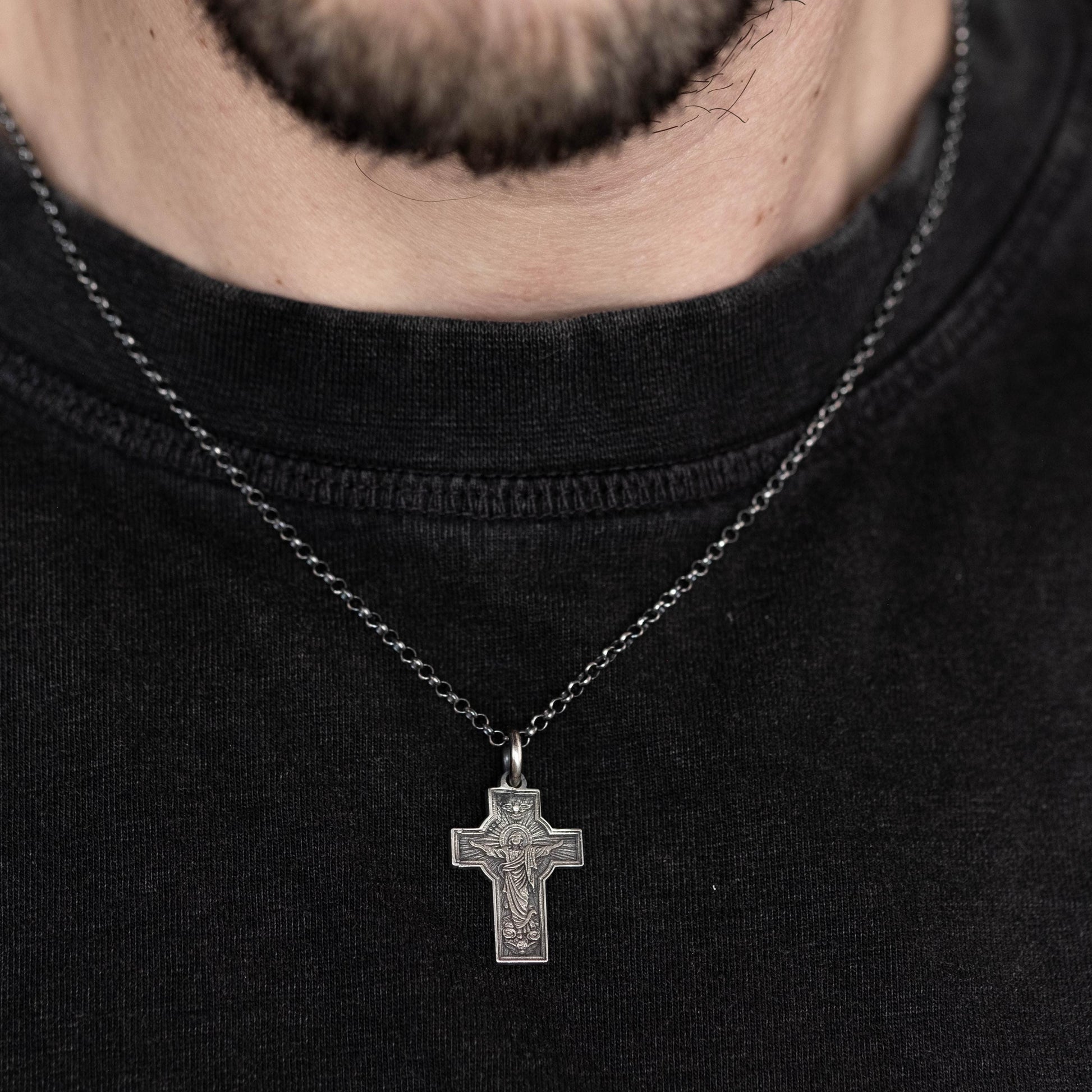 A silver cross pendant is hanging from a black shirt.