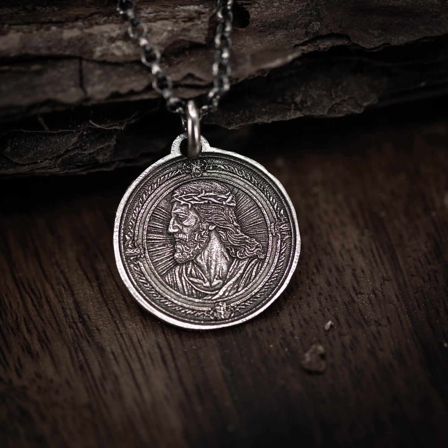 A silver-colored pendant featuring a detailed engraved image of a man's face, likely depicting a religious figure.