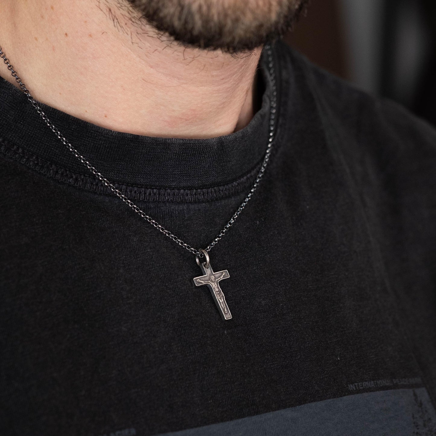 A silver cross pendant is hanging from a black t-shirt.