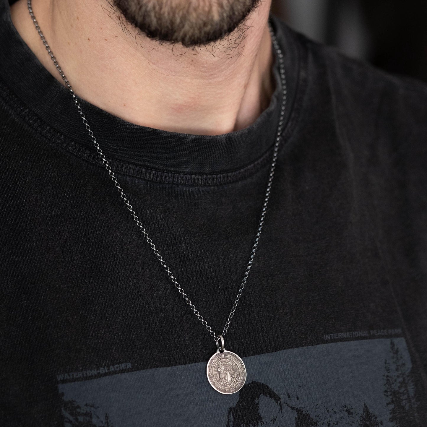 A close-up of a person wearing a black t-shirt with a silver chain necklace featuring a round pendant.