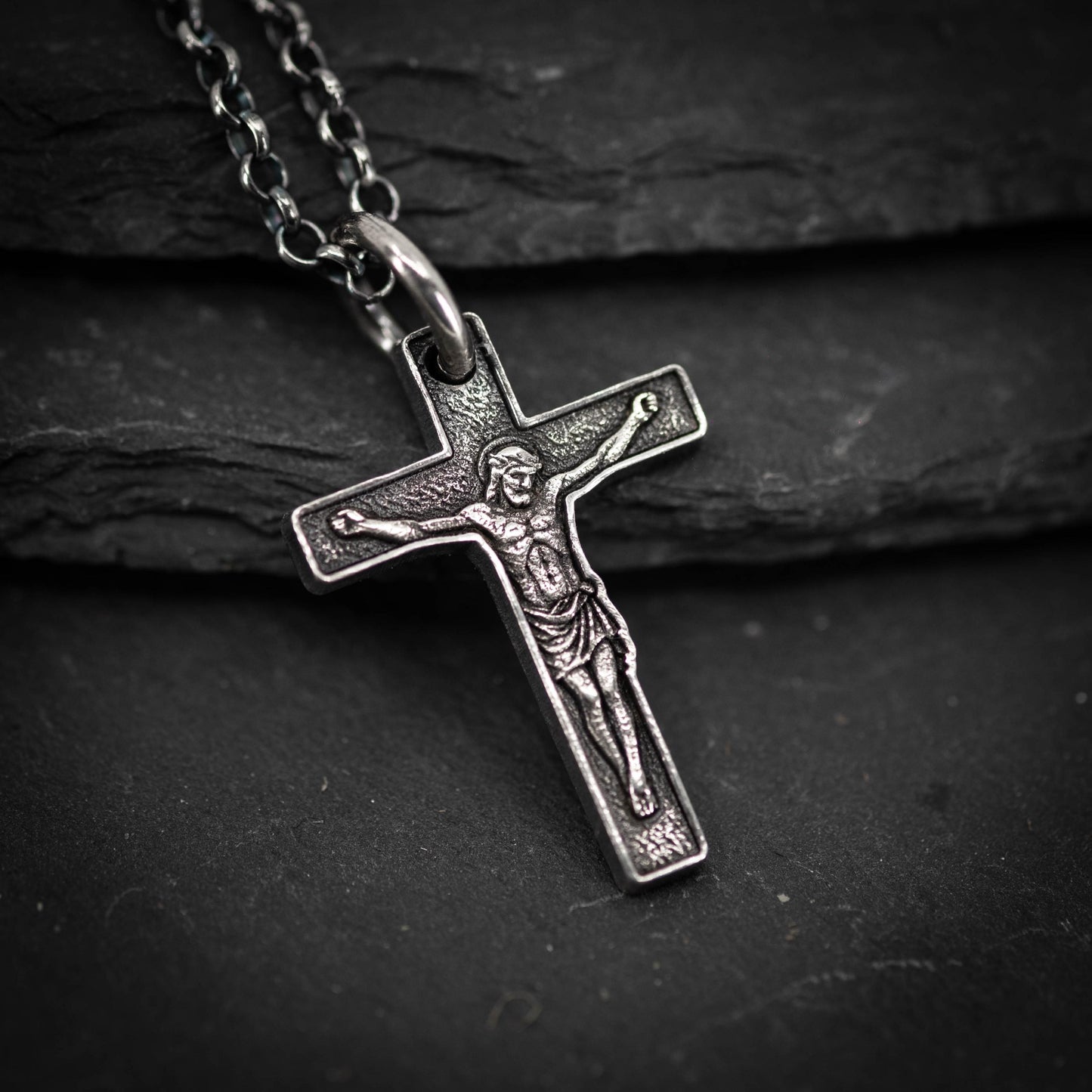 A silver cross pendant with a detailed engraved image of Jesus Christ on it, resting on a dark surface.