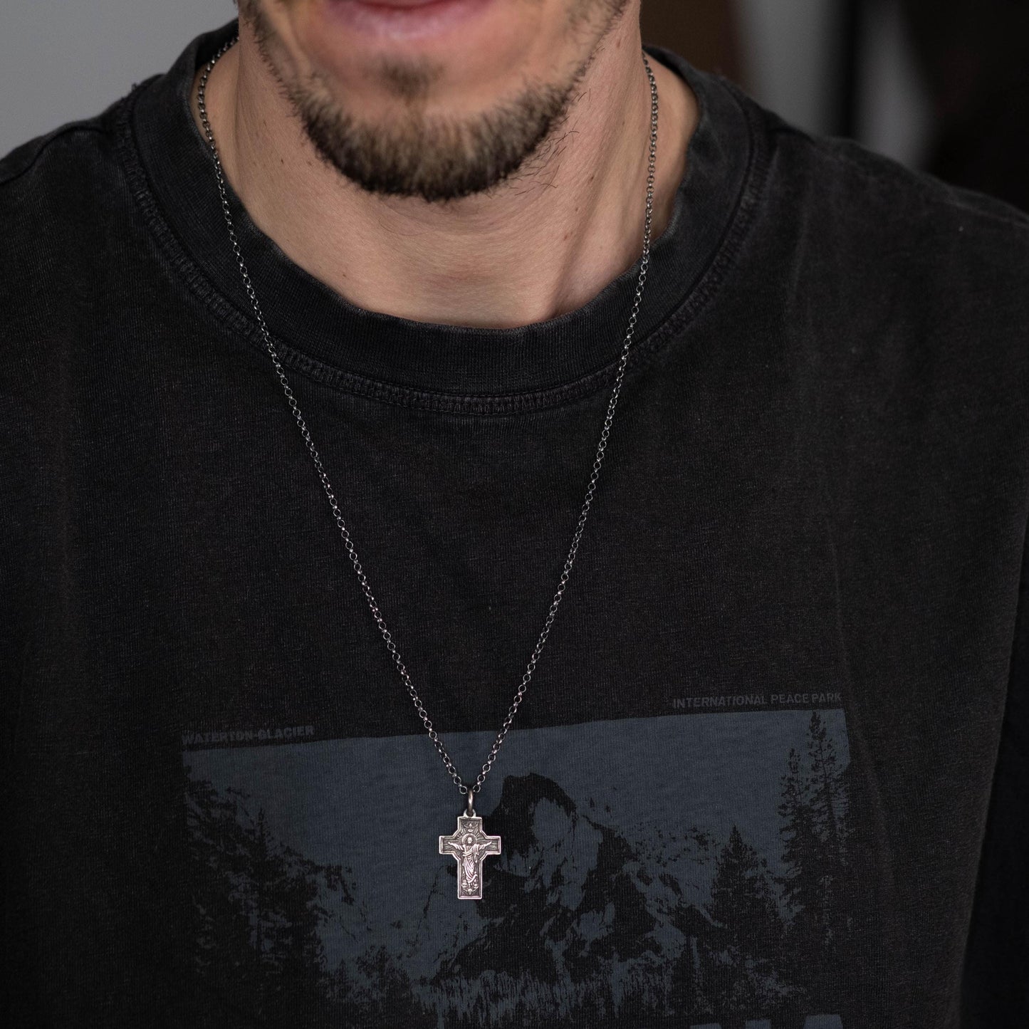 A close-up of a person wearing a black t-shirt with a graphic design and a silver cross necklace.