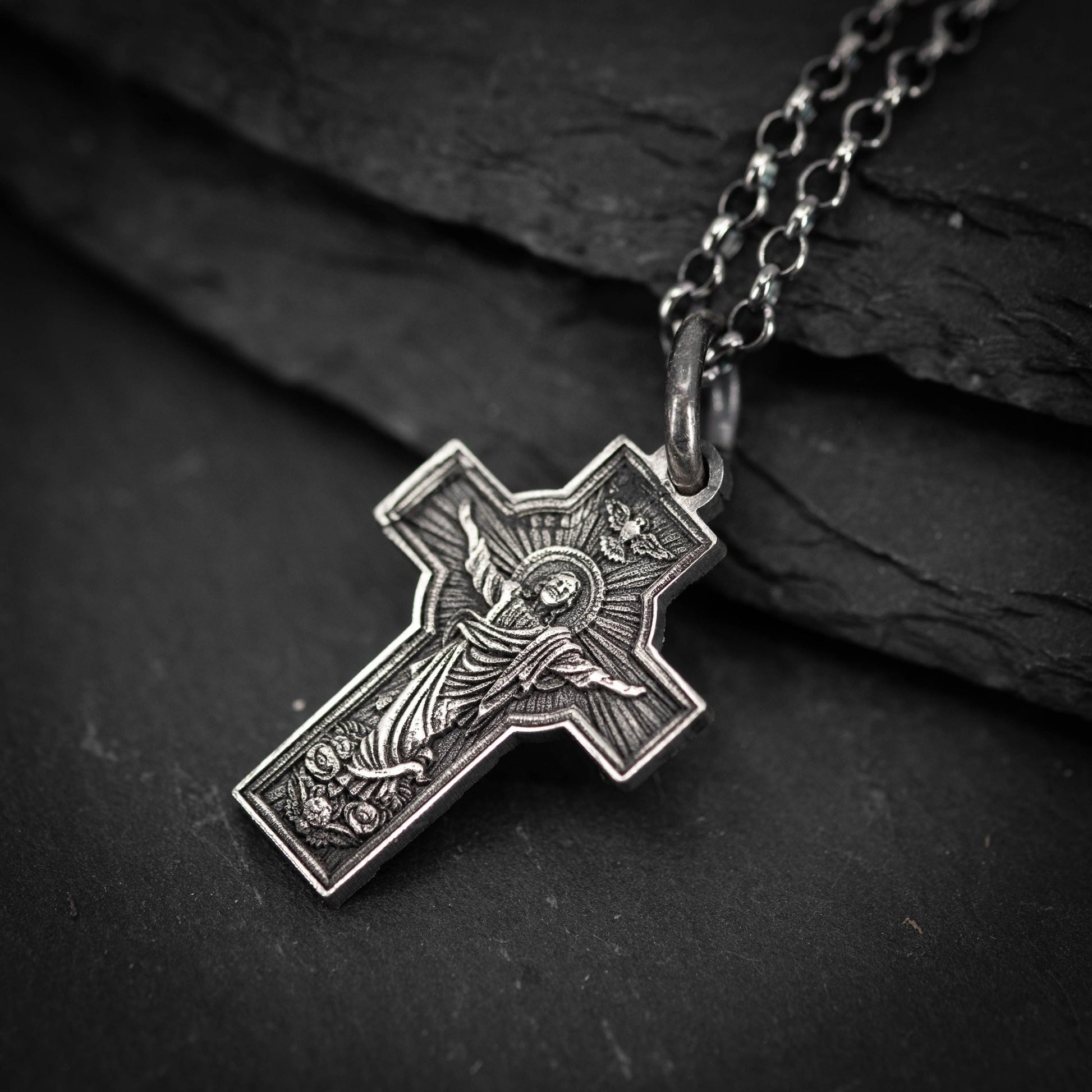 A silver cross pendant with an intricate design, resting on a dark surface.