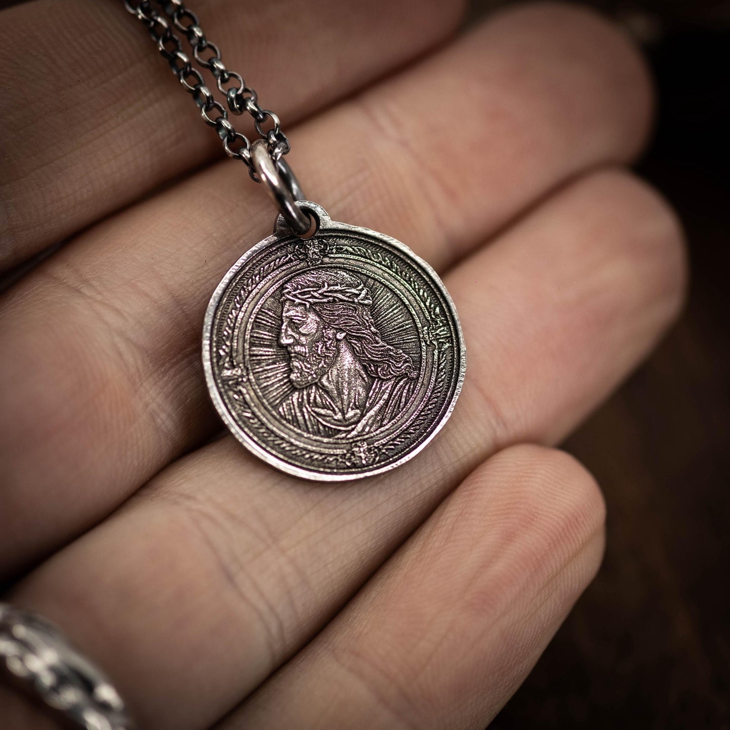 A hand holding a silver-colored pendant featuring an engraved image of a person's face.