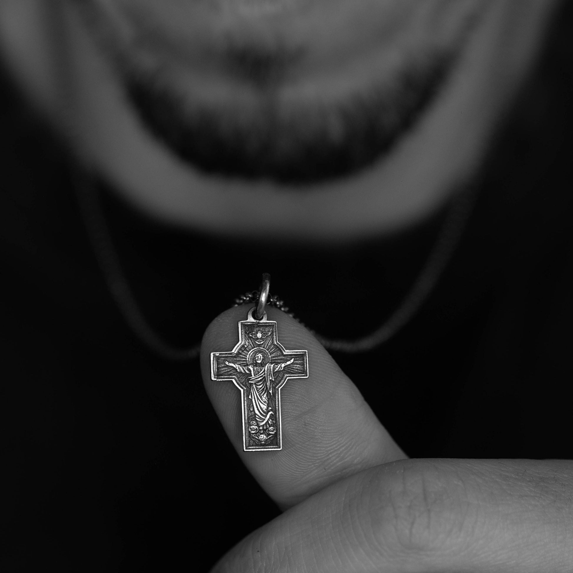 A person's hand holding a small cross pendant against a dark background.