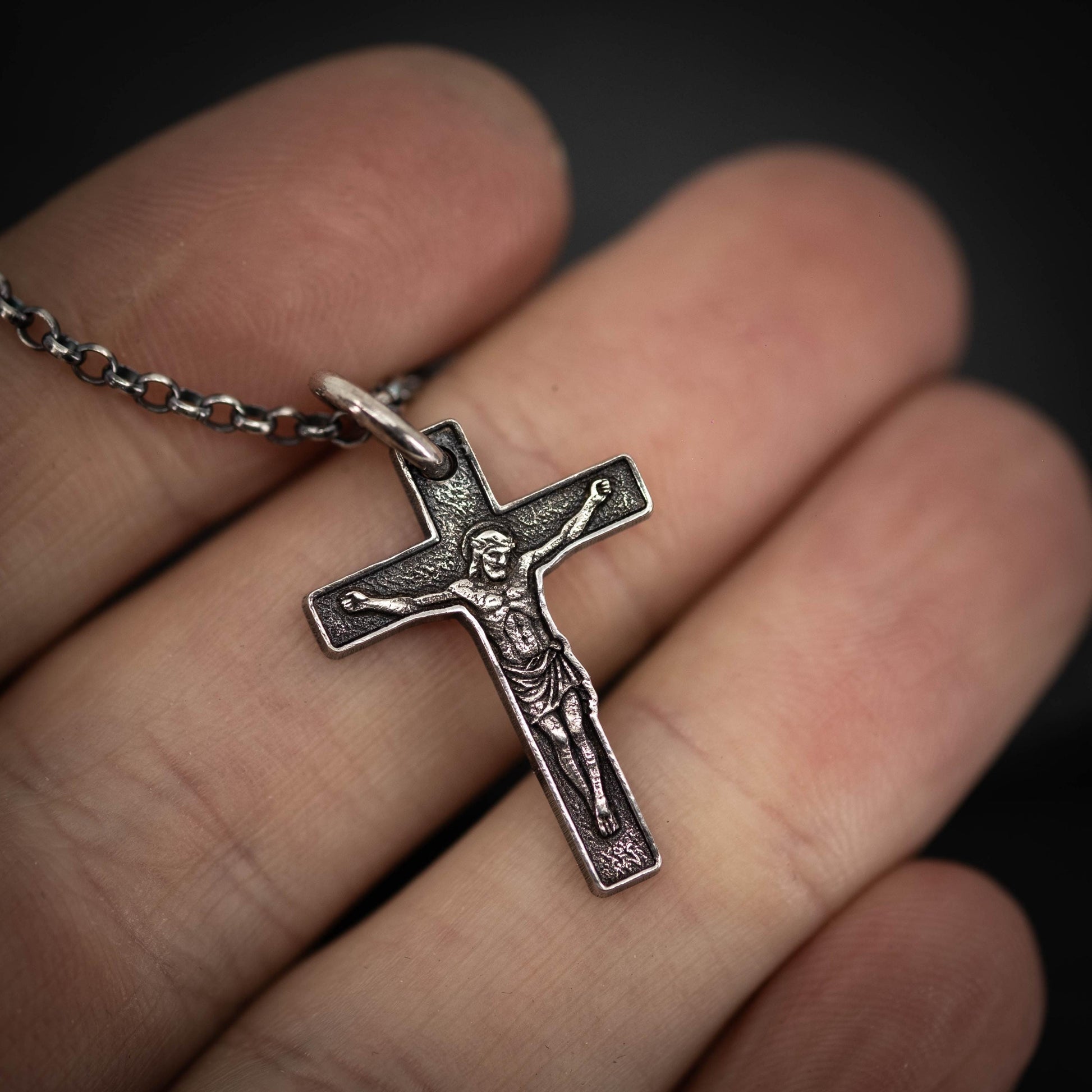 A close-up image of a person's hand holding a silver cross pendant.