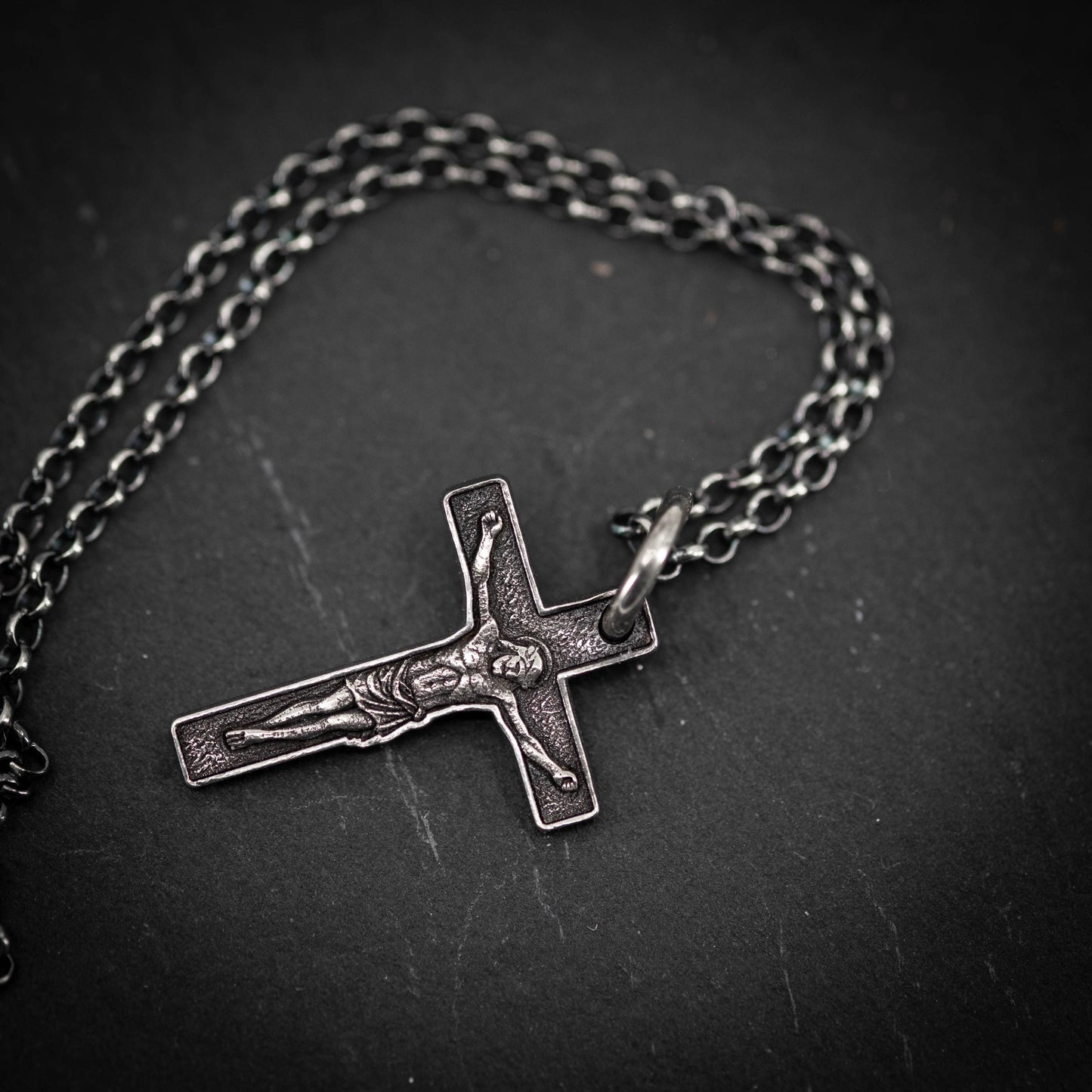 A silver cross pendant with a crucifix design is shown against a dark background.