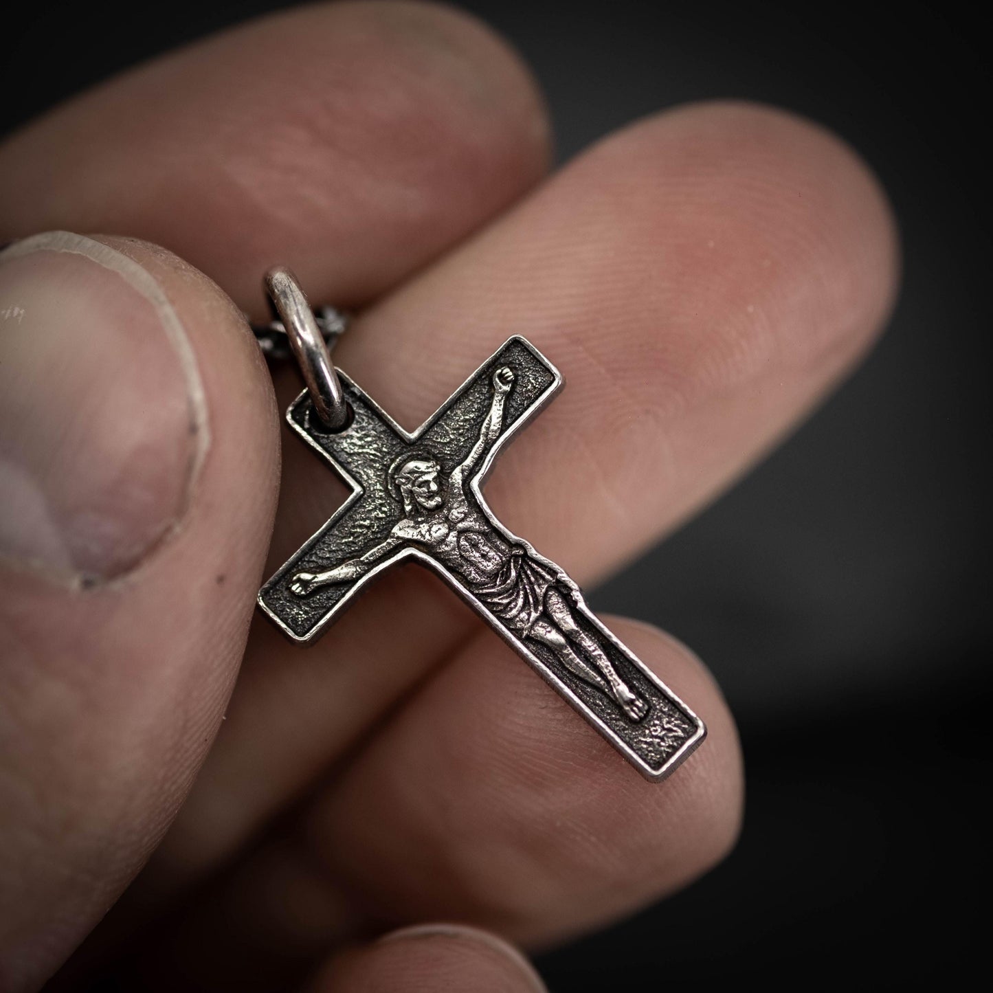 A close-up image of a person's hand holding a silver cross pendant.
