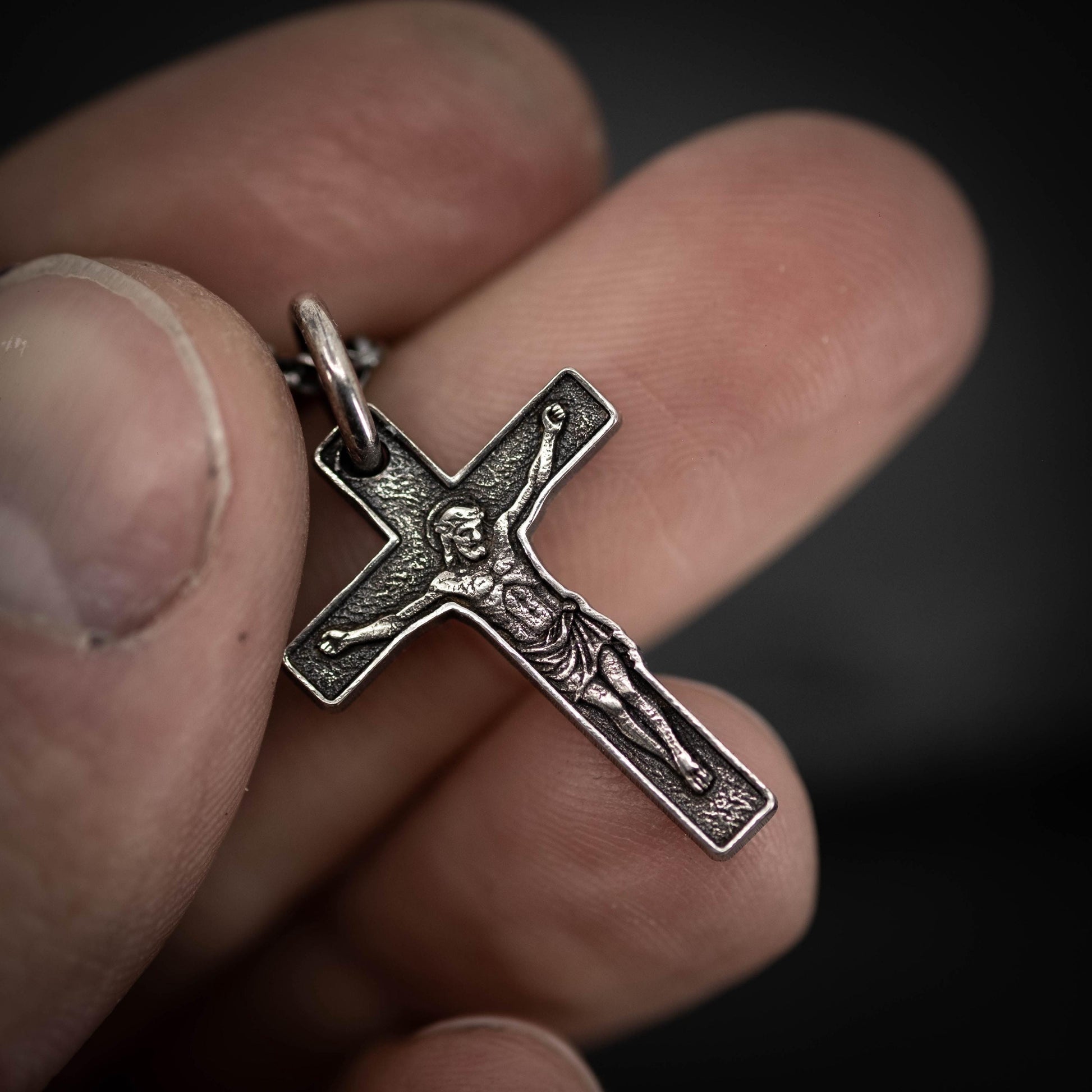 A close-up image of a person's hand holding a silver cross pendant.