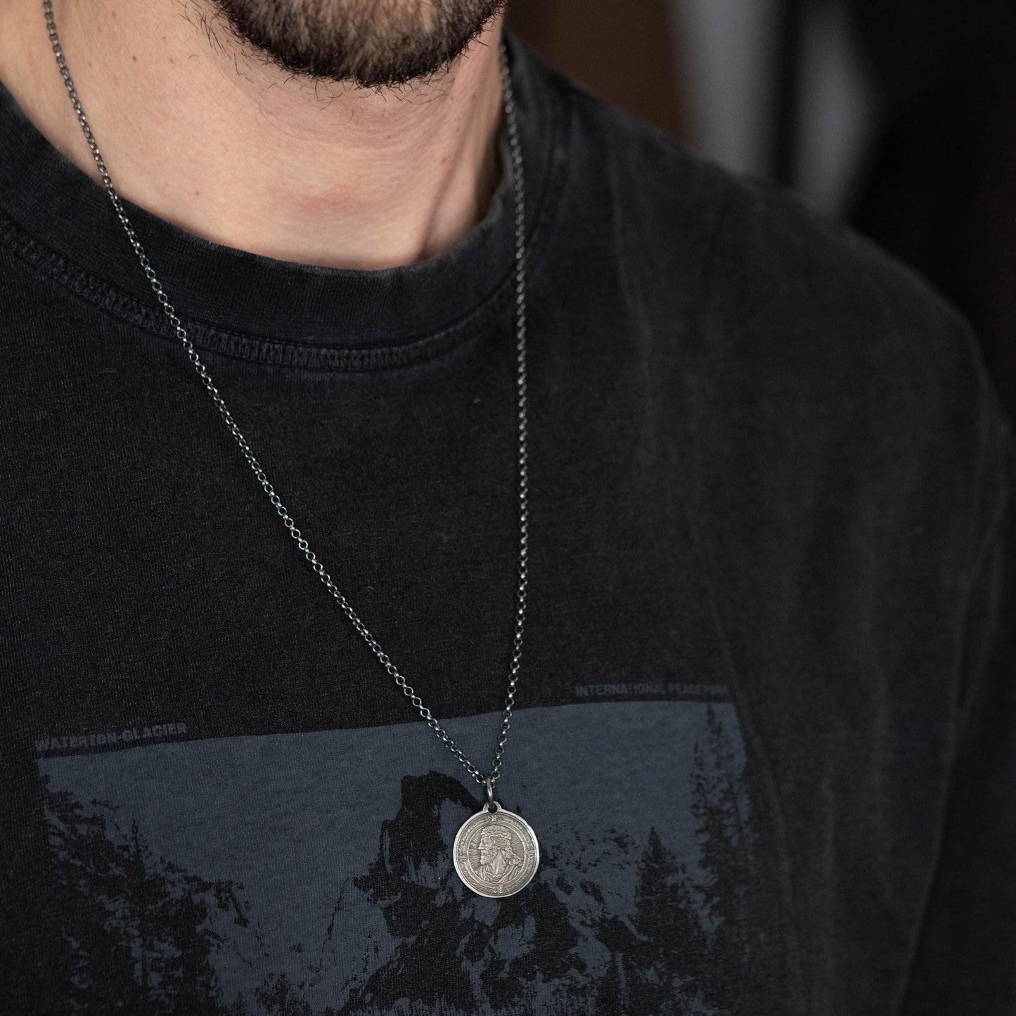 A close-up of a person wearing a black t-shirt with a graphic design and a silver necklace with a pendant.