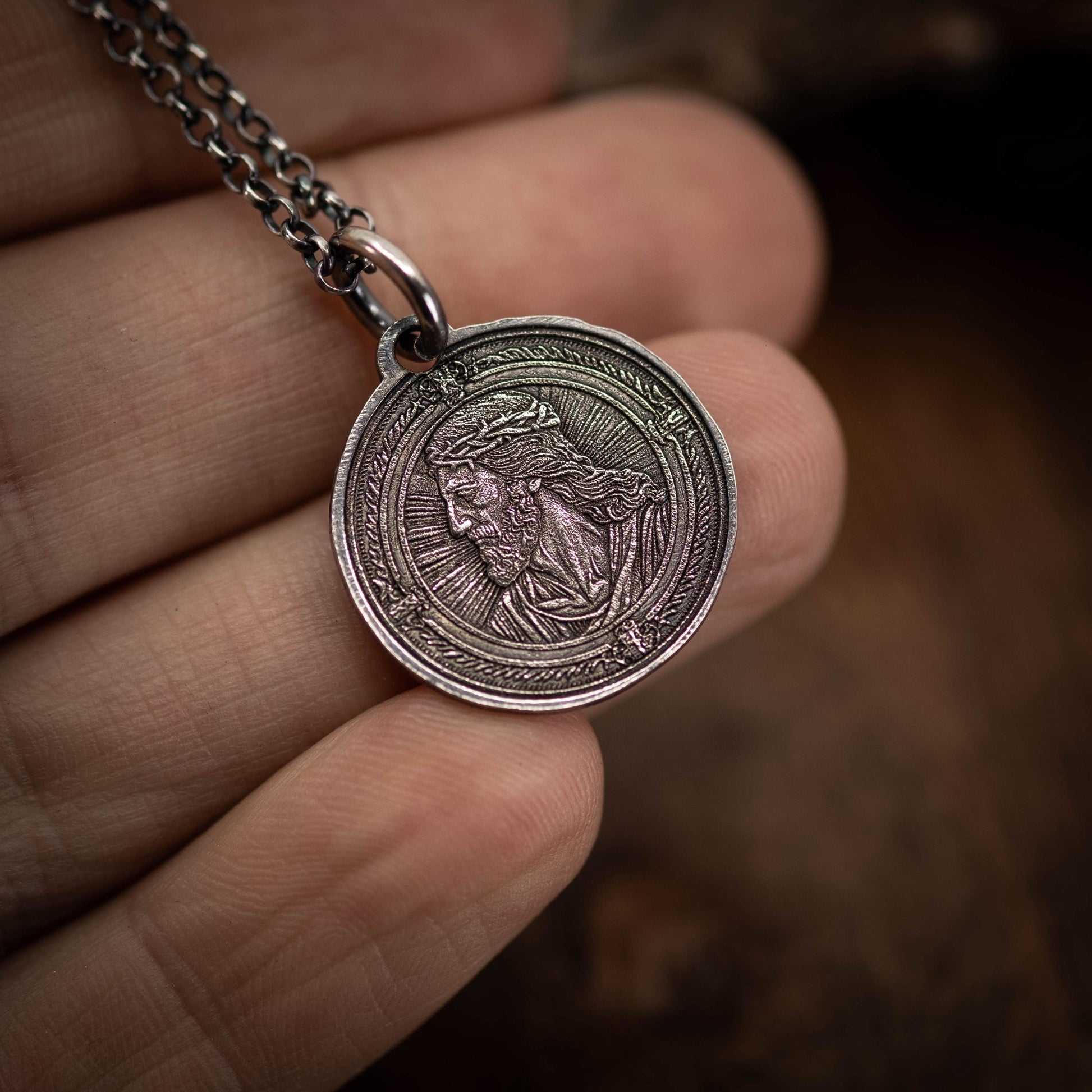 A hand holding a silver-colored pendant featuring an engraved image of a person's face.