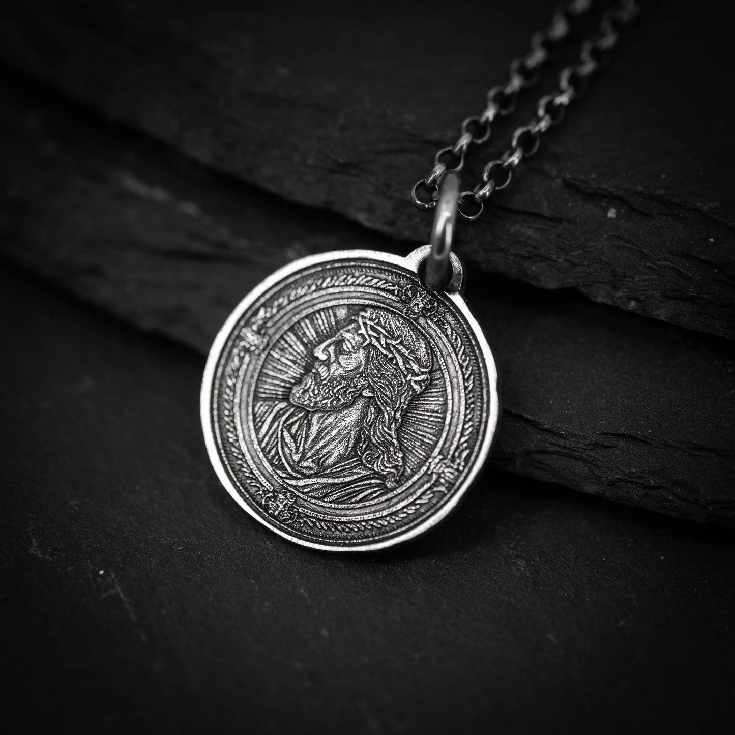 A close-up view of a silver pendant featuring an engraved image of a person's face, likely a religious figure.