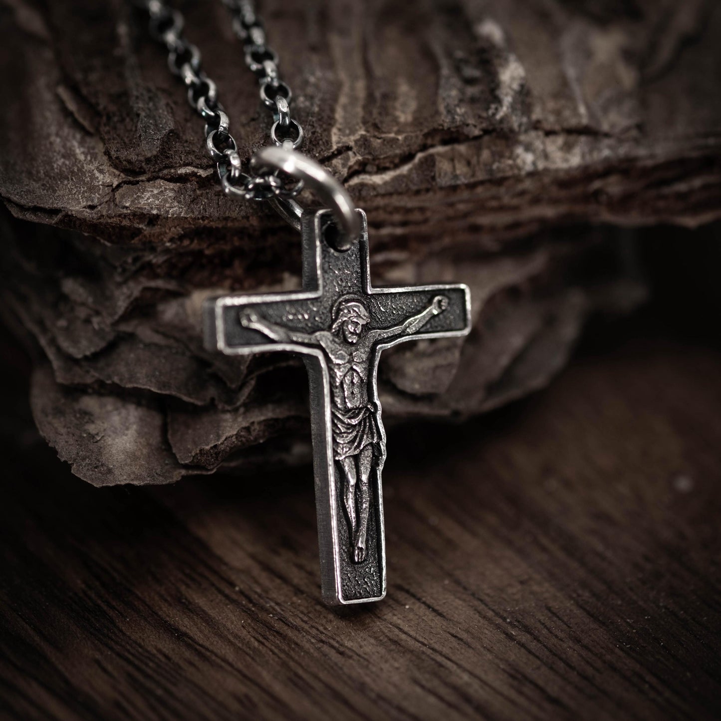 A silver cross pendant with a religious figure engraved on it, resting on a wooden surface.